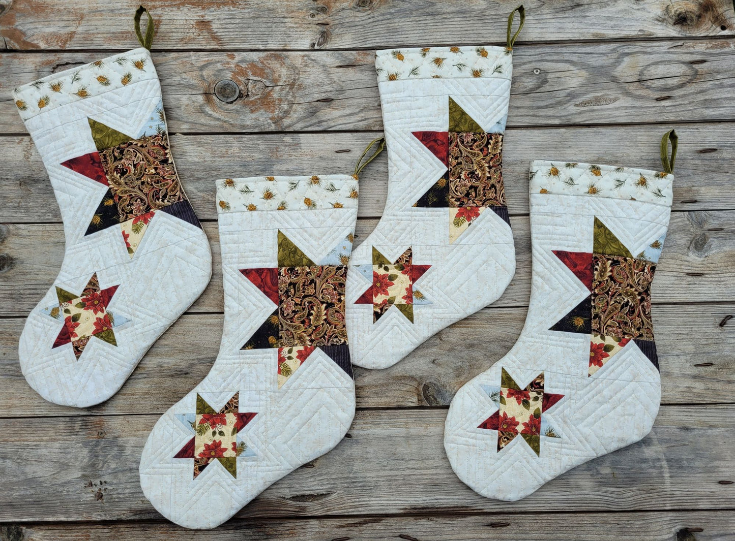 Four handmade quilted Christmas stockings with star and geometric patchwork designs, displayed on a rustic wooden plank background.