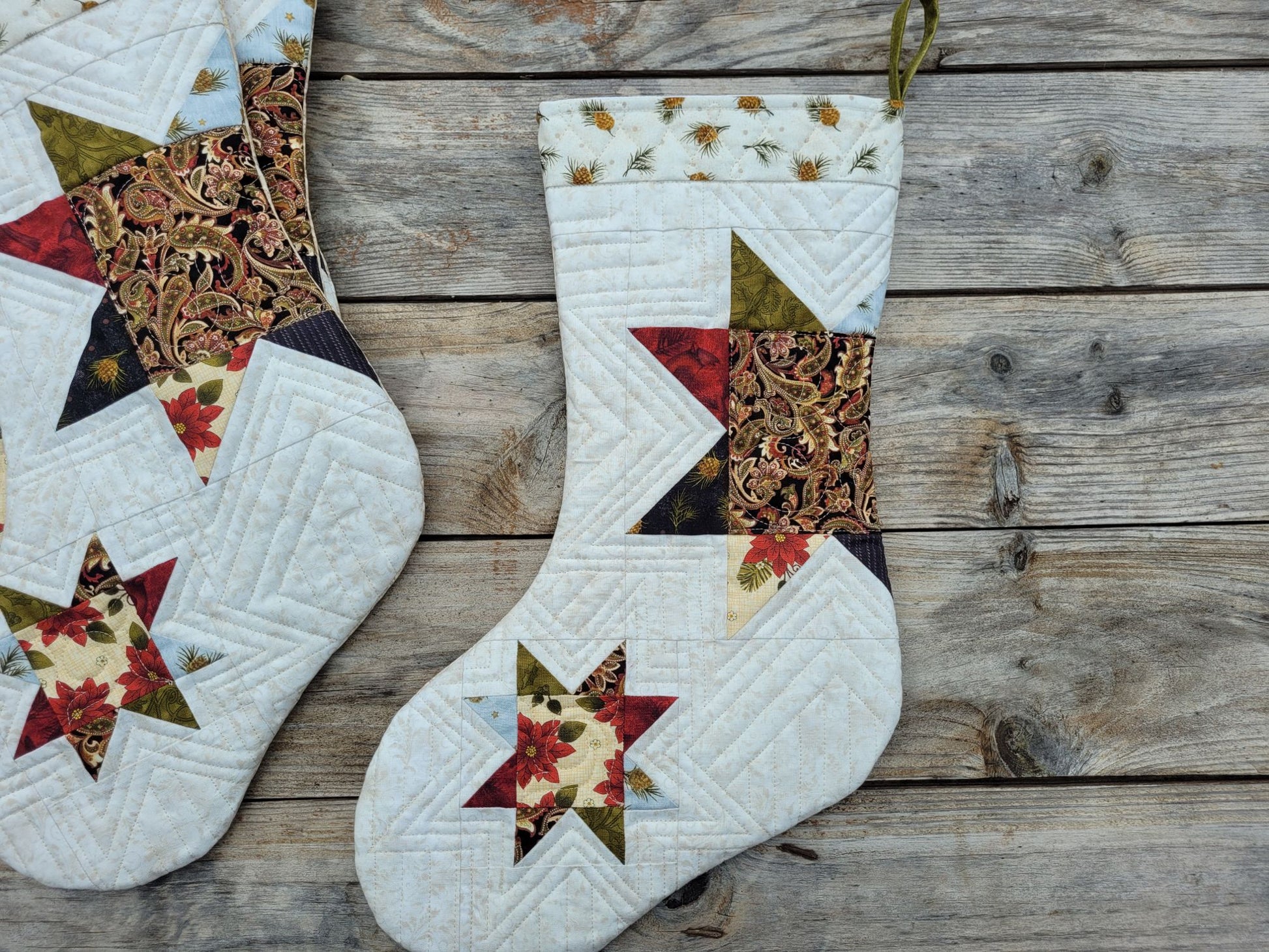 Handmade quilted Christmas stockings with star and floral patchwork designs, displayed on a rustic wooden plank surface.