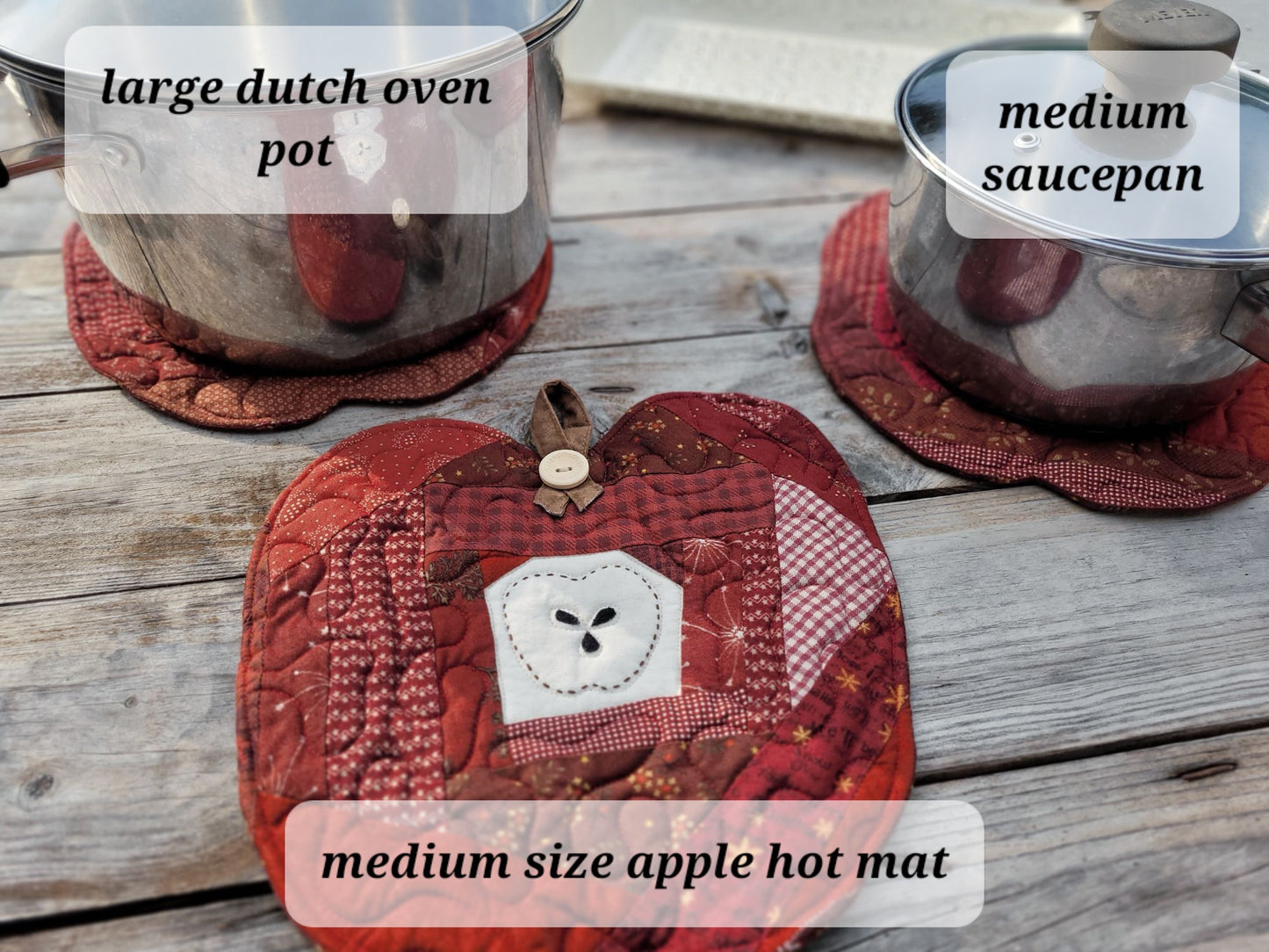 A quilted red apple-shaped hot mat with a white hand-stitched apple outline patch in the center, displayed on a rustic wooden table alongside a large Dutch oven pot and a saucepan, each resting on a matching red trivet. Text overlays identify the items.