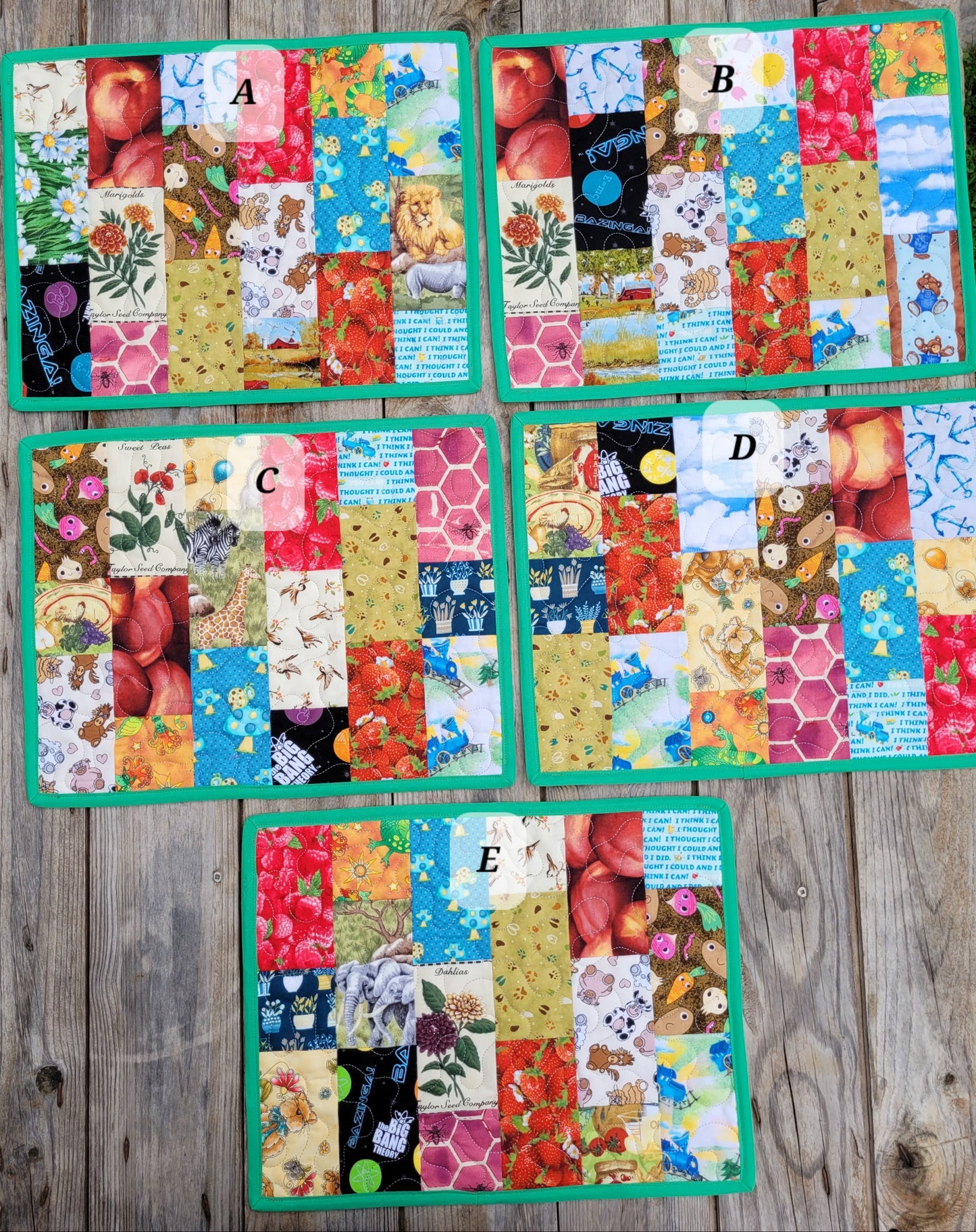 Five colorful patchwork quilted placemats with green borders are arranged on a rustic wooden surface. Each placemat features a different whimsical print patch including animals, fruits, flowers, and text, with a white circular label showing the letter A, B, C, D, or E.