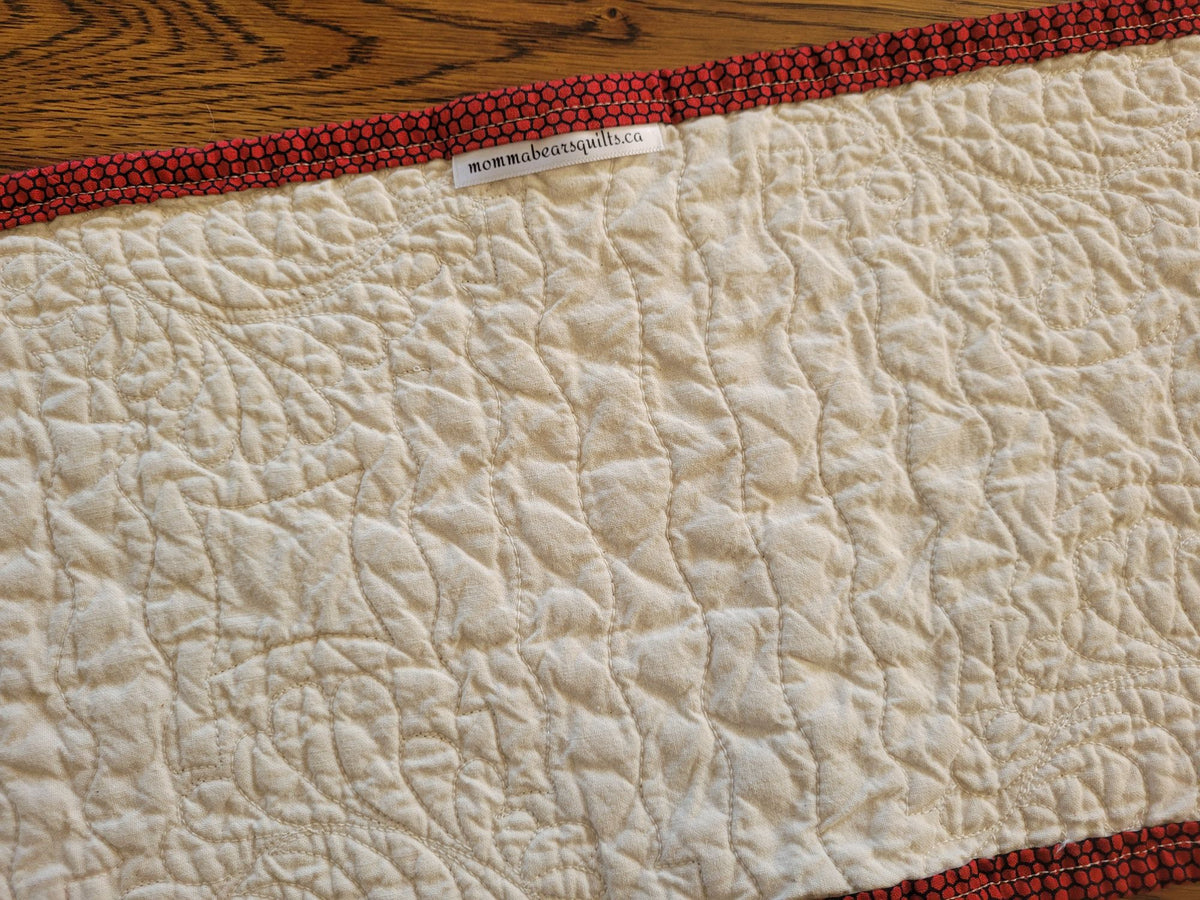Showing the back of the small quilted table runner with brand label on a wooden table.