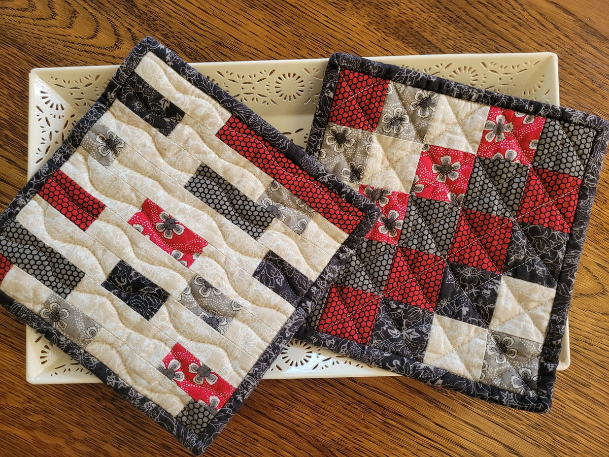 Showing two coordinating quilted pot holders on a white decorative tray on a wooden table.