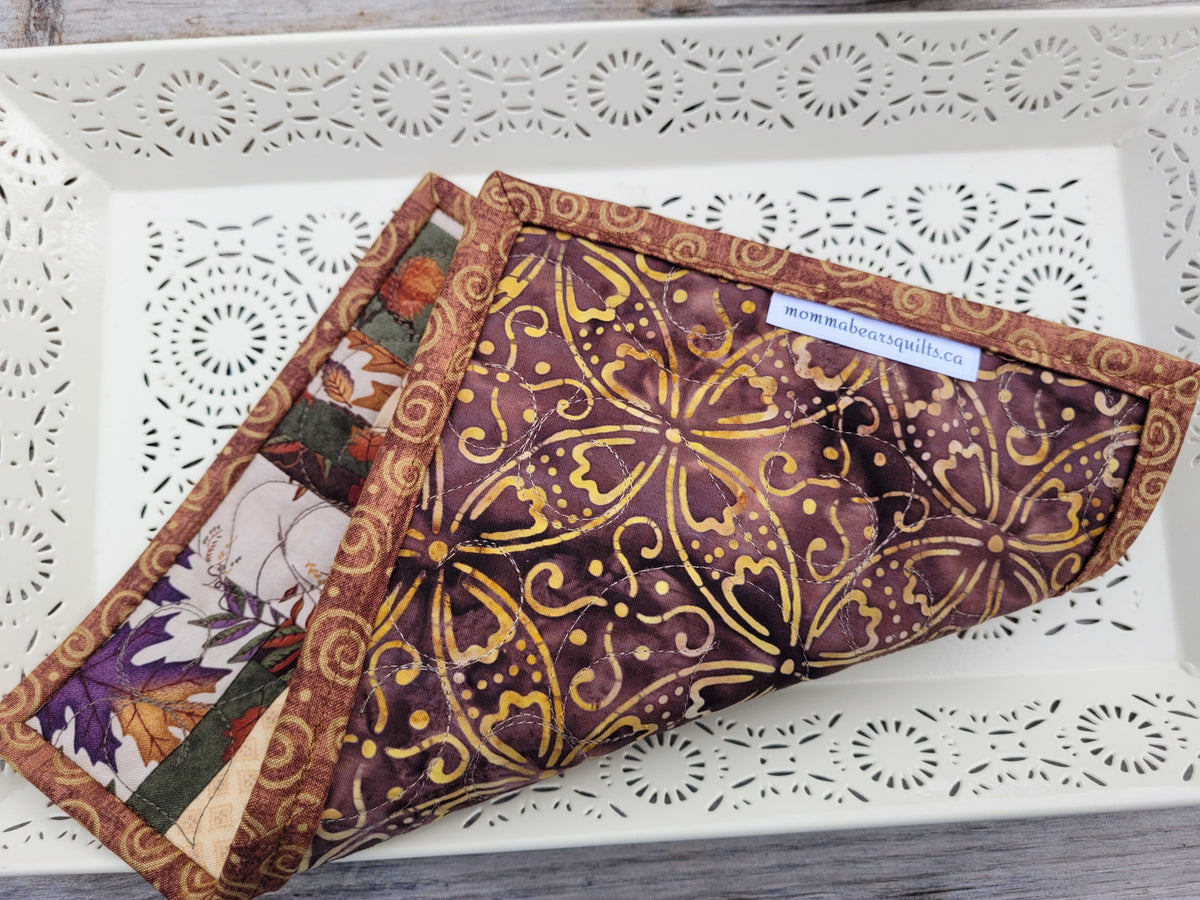 A mini fall scrap quilt folded to show the backing of a brown and gold batik-style floral fabric, displayed on a white decorative tray.