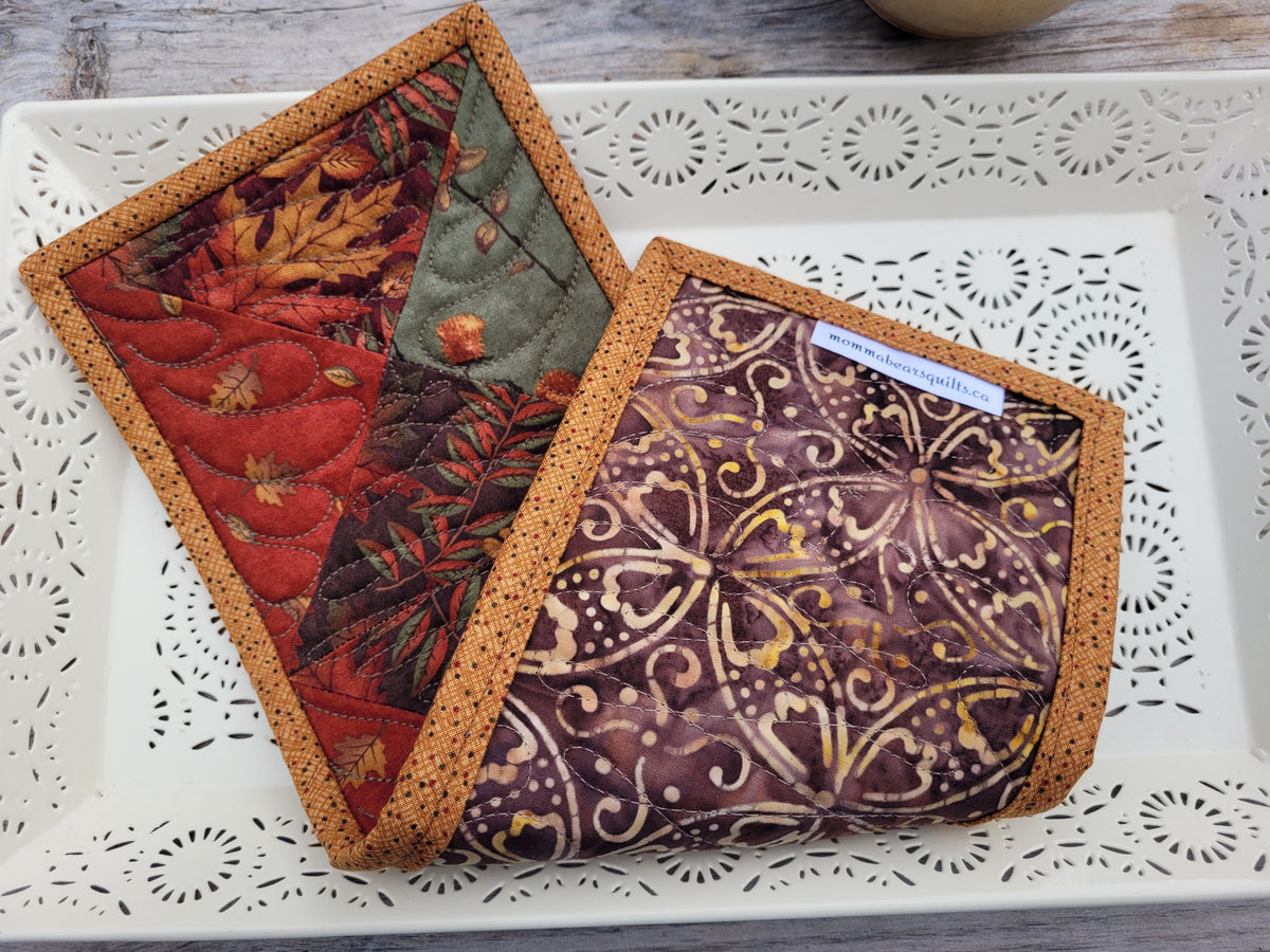 The fall mini quilt is folded to show the backing, which is a batik style fabric in brown and gold colours. Styled on a white decorative tray.