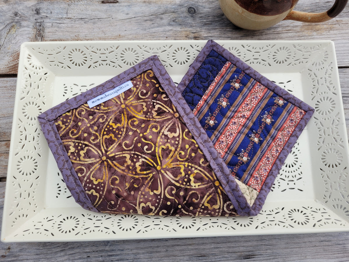 A small quilt is folded to show the backing, which is a batik style fabric in brown and gold colours. Styled on a white decorative tray.