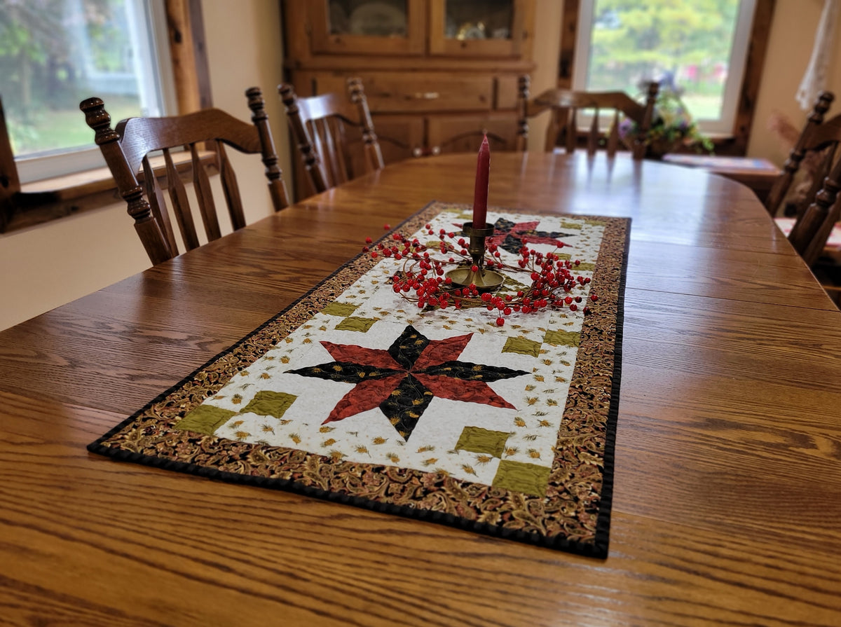 Christmas table runner, with a candle centrepice surrounded by red berries, is shown on a wood table in a diningroom setting.