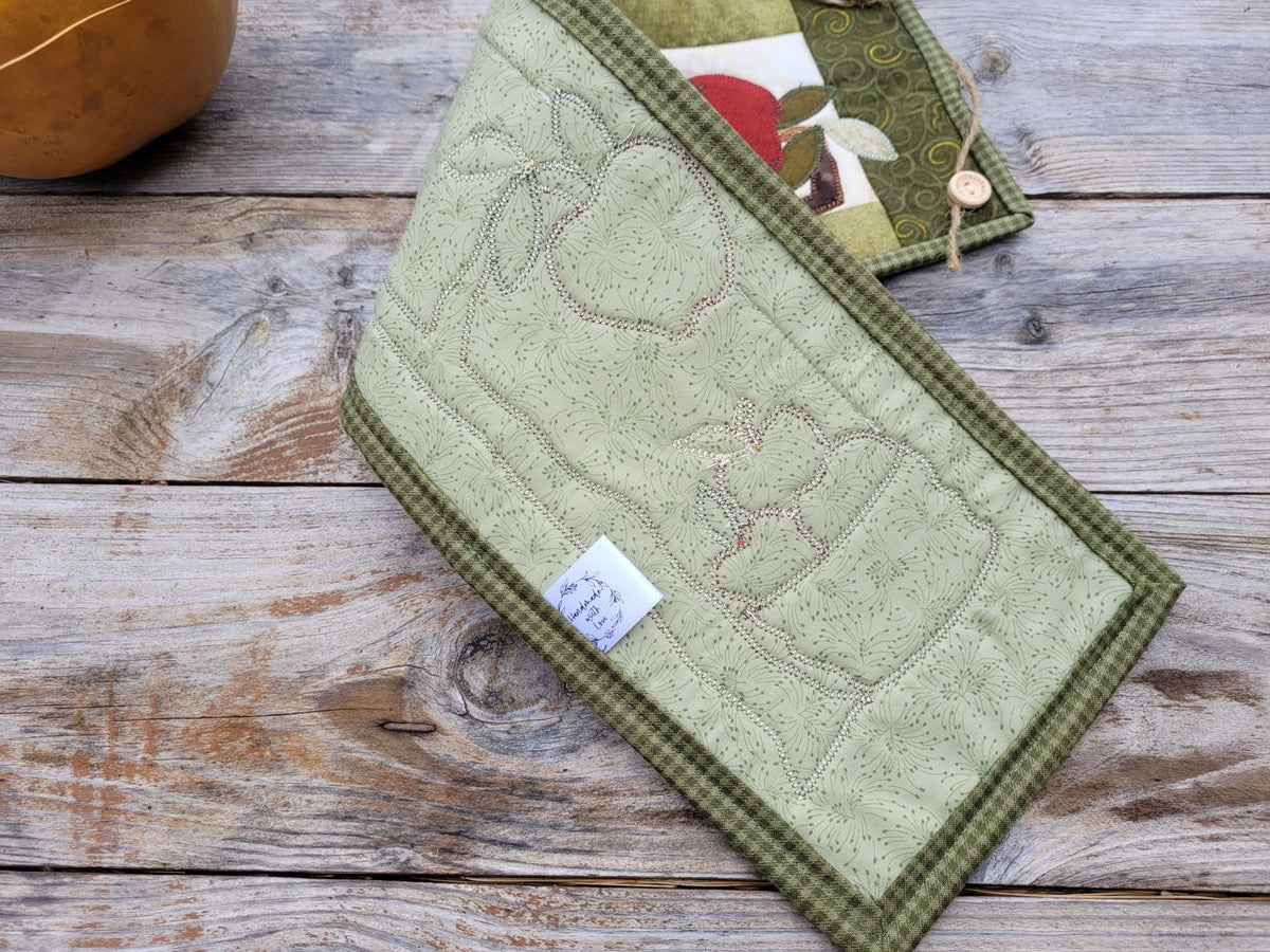 The narrow wall quilt is folded to show the green backing and stitches, on a weathered wooden table. 