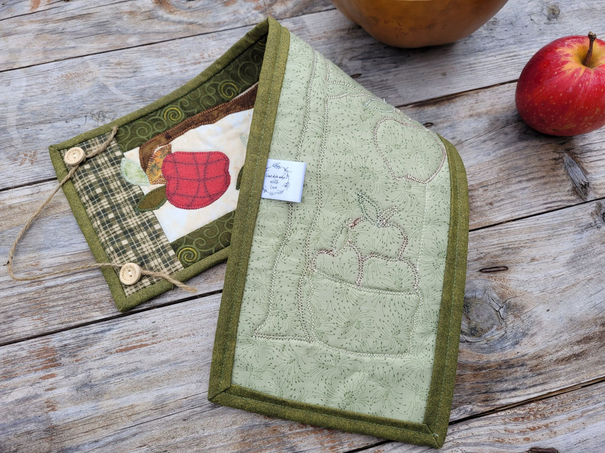 The skinny wall quilt is folded to show the green backing and stitches, on a weathered wood table with a red apple nearby.