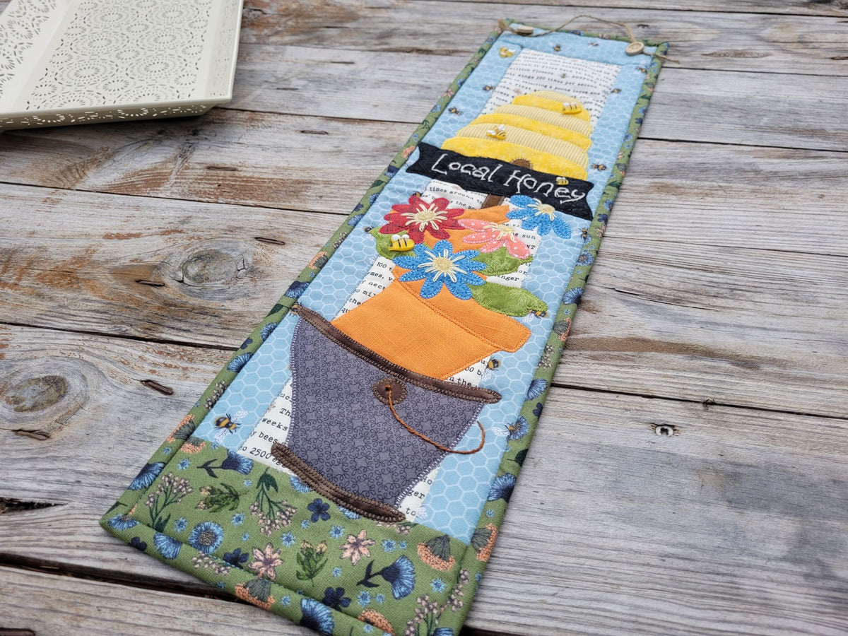 An angle view of the skinny wall quilt laid on a weathered wood table with a white decorative tray partially visable in the upper left.