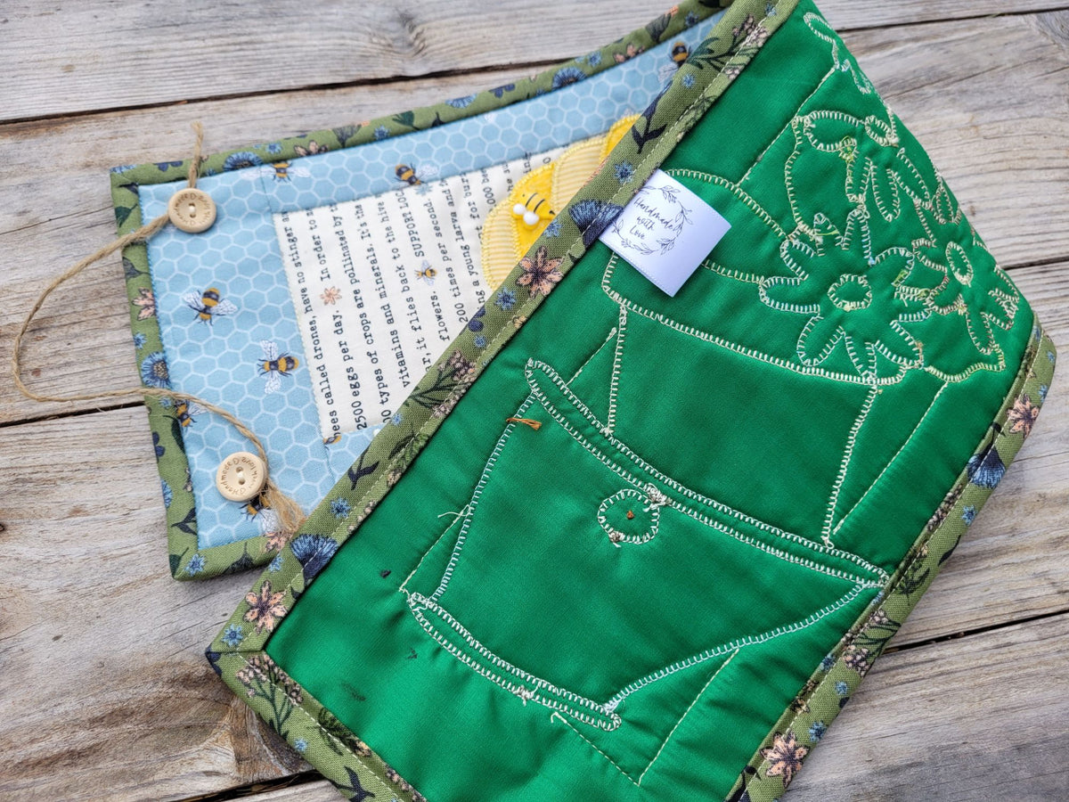A narrow wall quilt is folded to show the green backing with stitches on a weathered wood table.