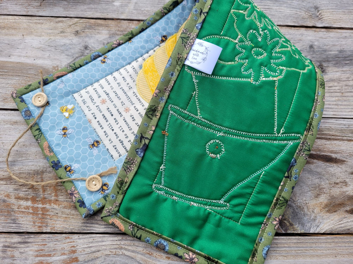 The narrow wall quilt is folded to show the green backing with stitches, shown on a weathered wood table.