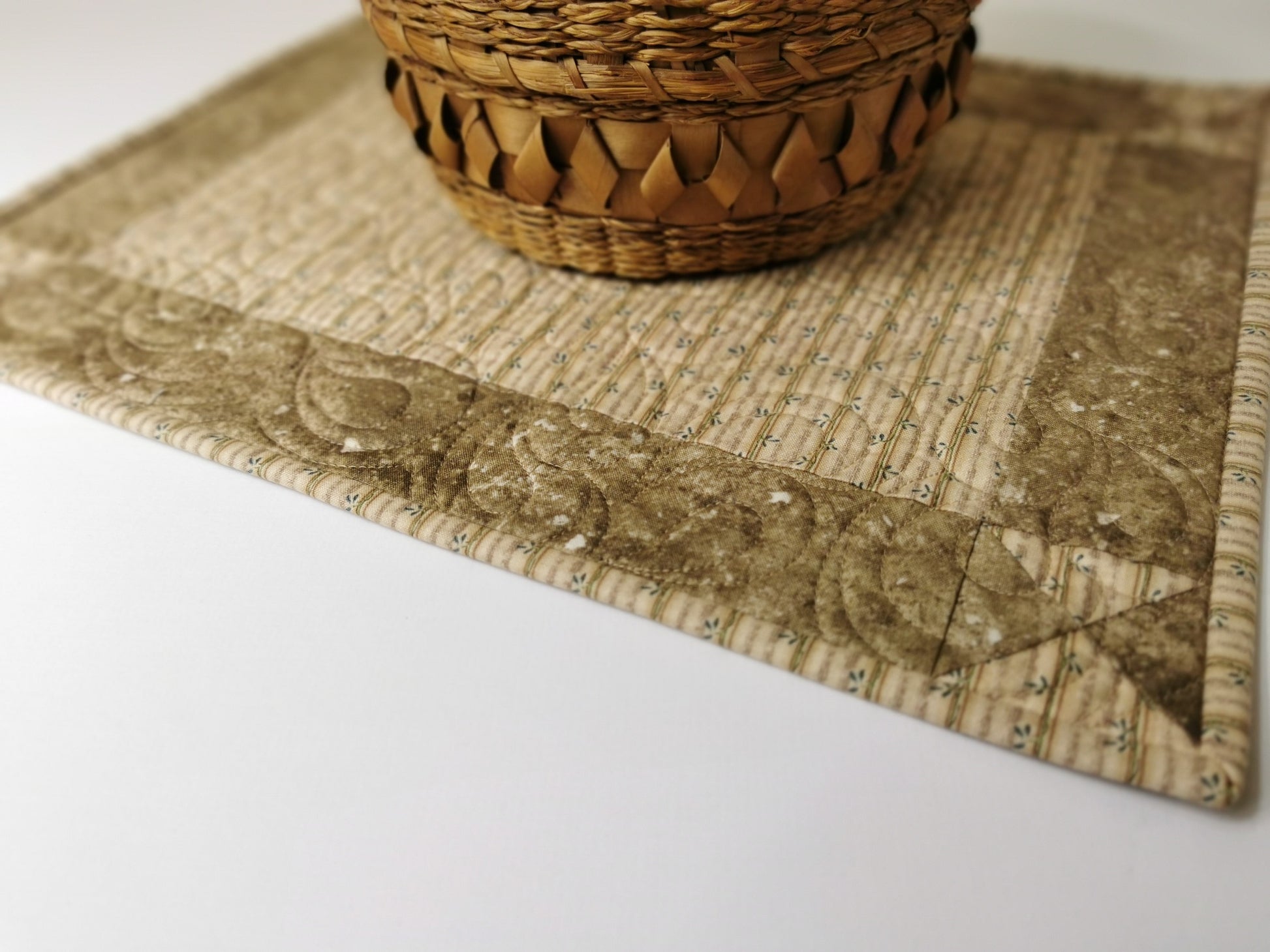 Quilted placemat is shown with a wicker basket sitting on it. Neutral beige fabrics with simple piecing make these both pretty and practical.