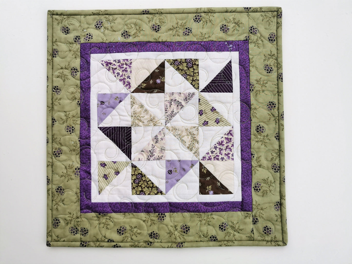 This square table topper has scrappy pinwheels in the center surrounded by a narrow purple border. Finished with a wider border in spring green with purple flowers. 