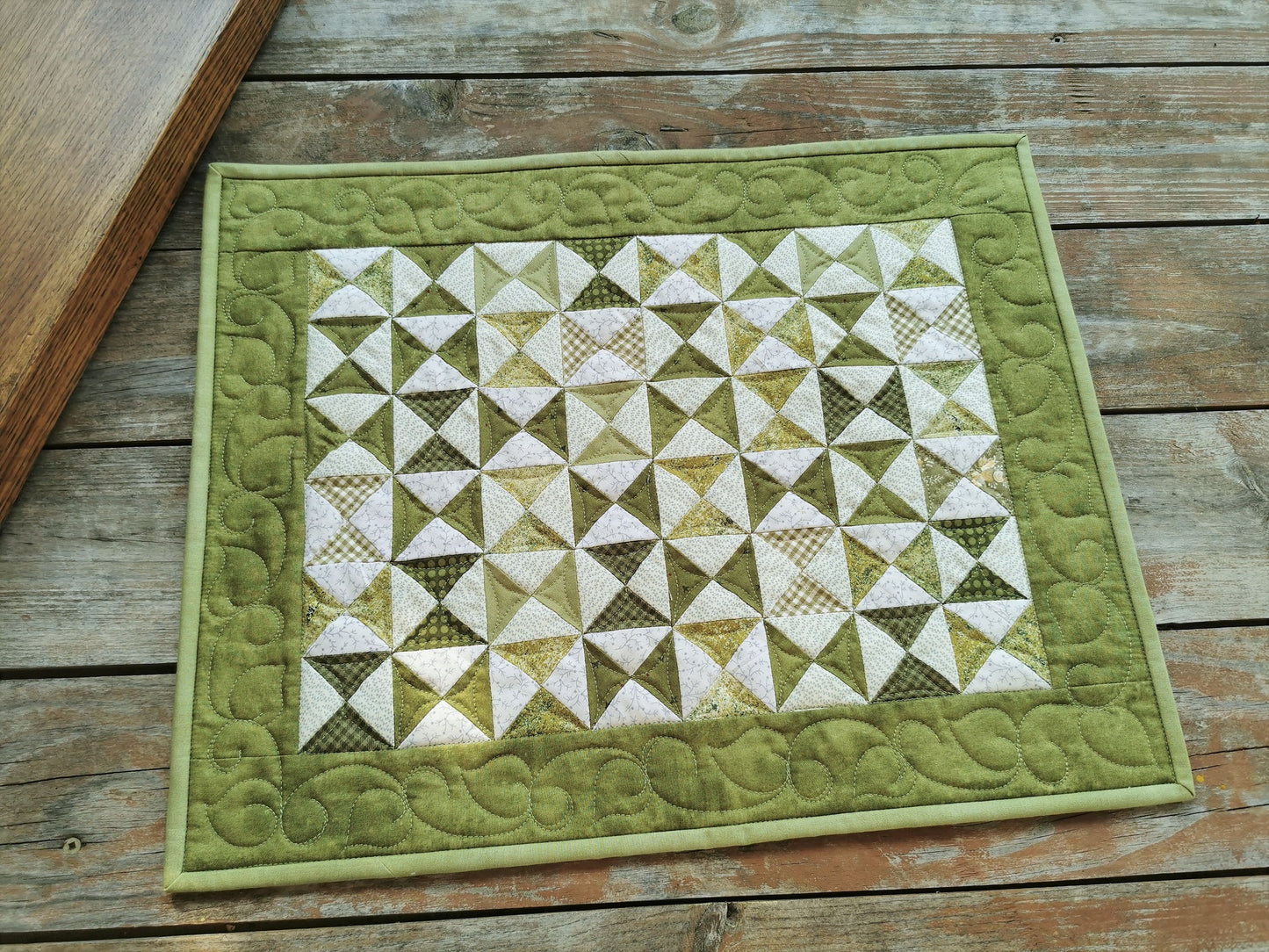 Small scrappy green triangles in hourglass shapes are surrounded by a solid tone on tone green border that has pretty custom quilting in a leafy vine pattern. 