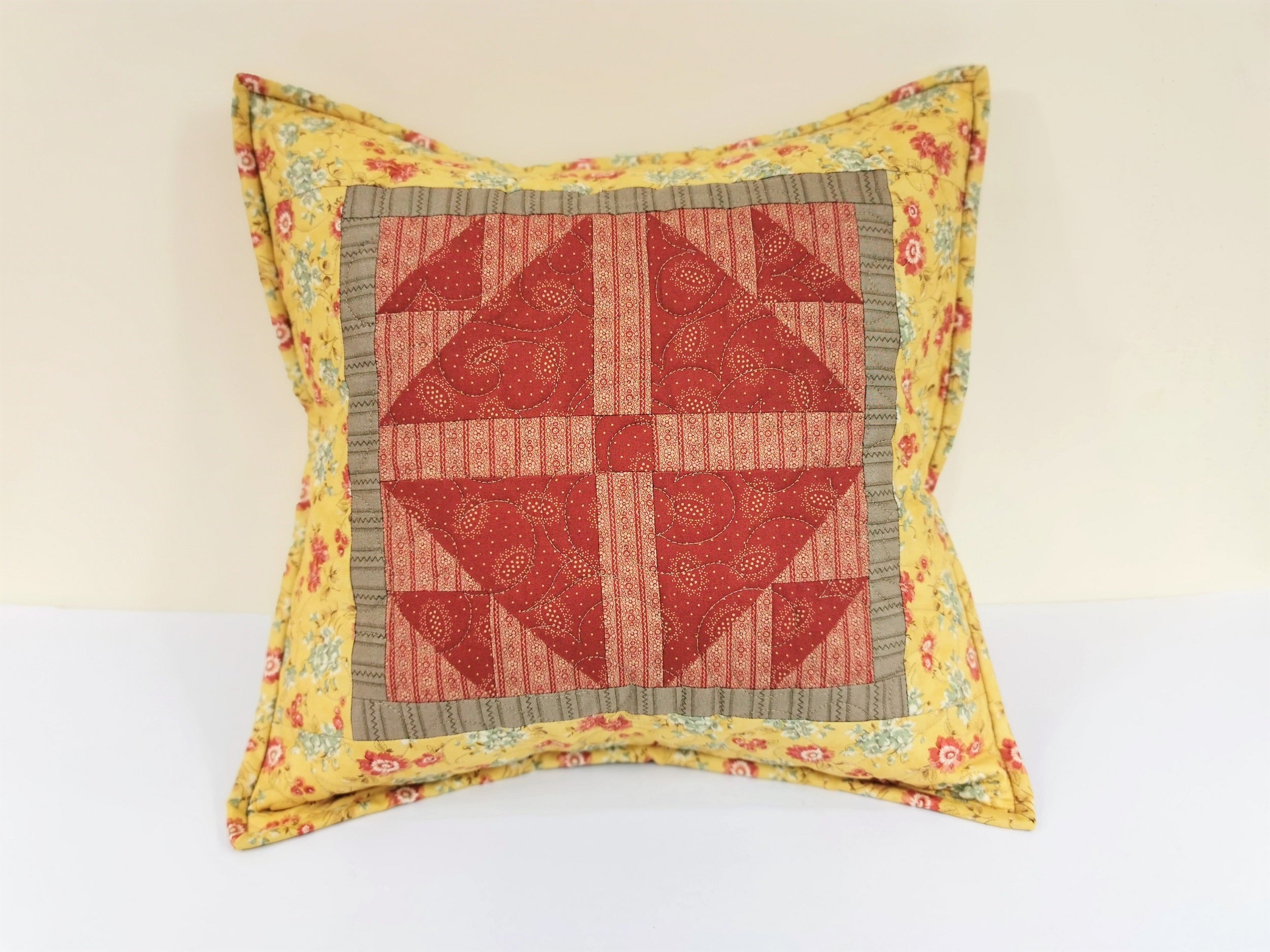 front view of  quilted pillow with two tone red center piecing surrounded by a drab brown border and finished with a coordinating yellow floral fabric