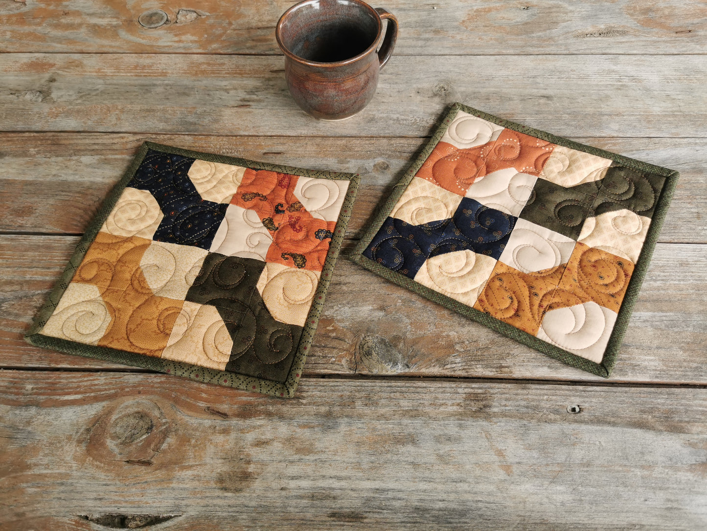 Each quilted patchwork potholder is made up of four bowties, all oriented in the same direction, each in a different color. Rustic country colors include forest green, navy, burnt orange, and gold.  Background is made with various  beige fabrics giving a scrappy look. Each potholder is bound with various forest green fabrics for another scrappy element. Fabric prints feature paisleys in various scales and designs. 