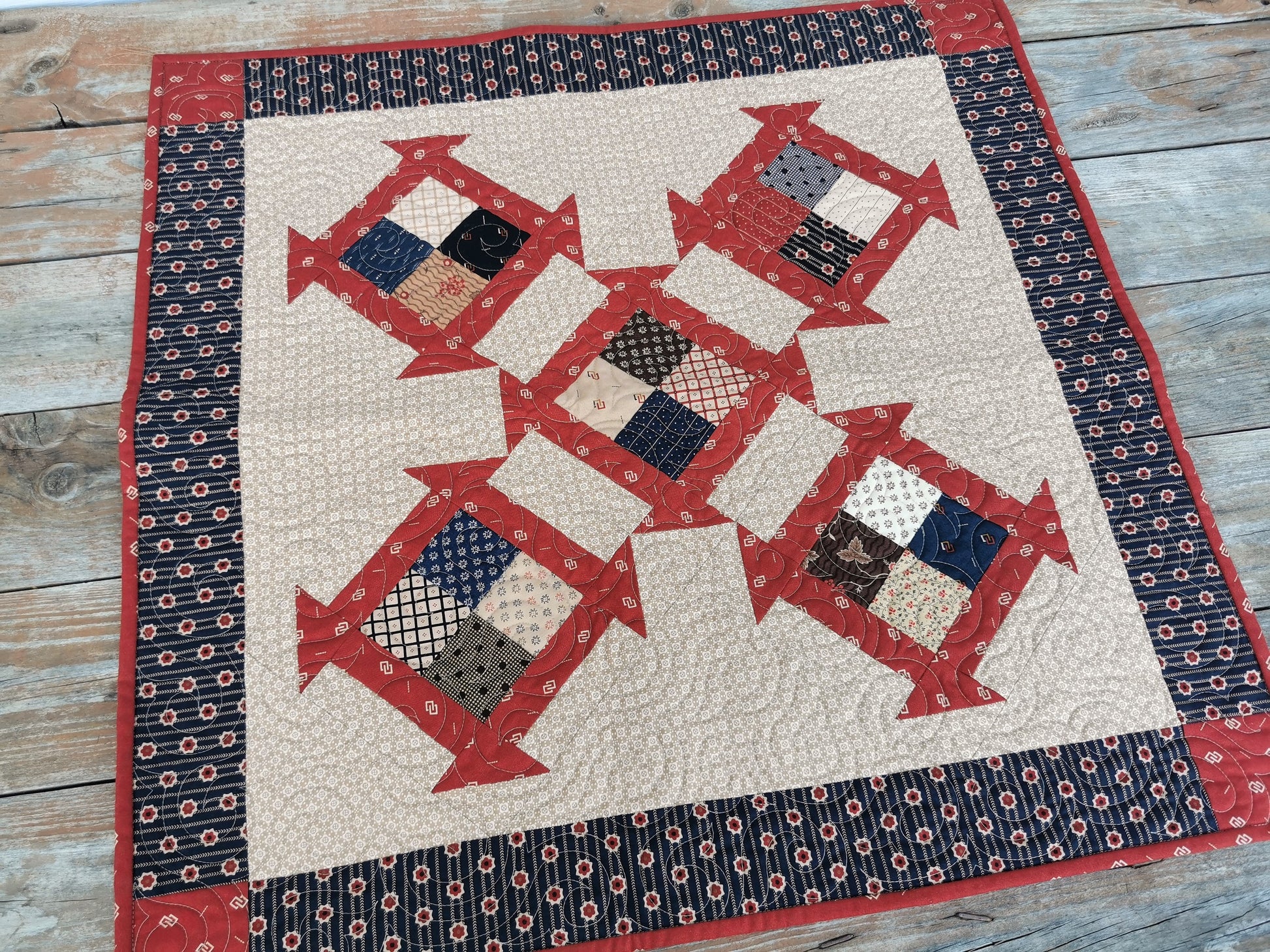 This square quilt  is made of  civil war fabrics in scrappy patchwork. Navy blue and red on a beige background are the main colors. Quilt patterns used are four patch and churn and dash. 