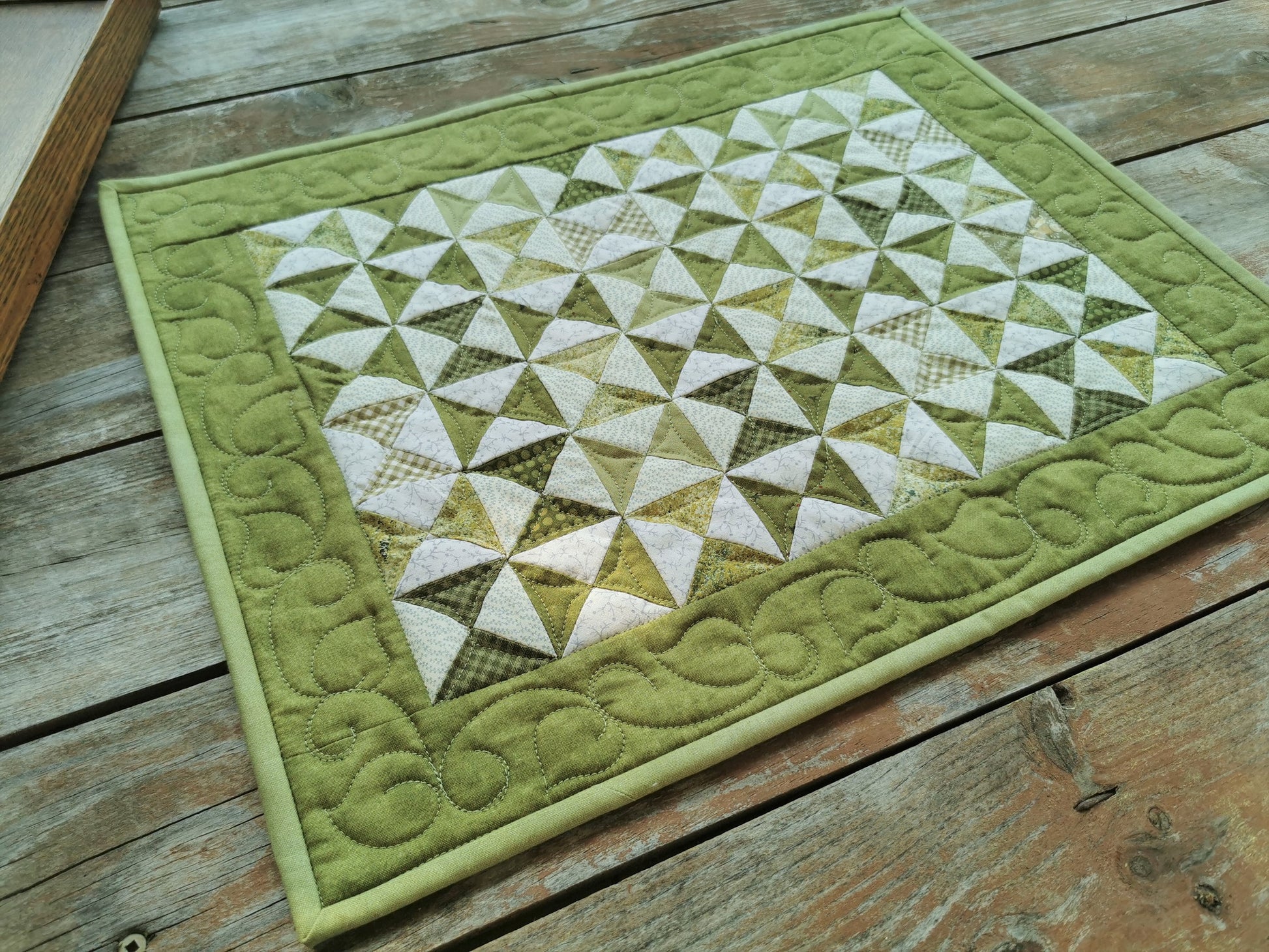 This quilted table runner has small scrappy green triangles in hourglass shapes are surrounded by a solid tone on tone green border that has pretty custom quilting.