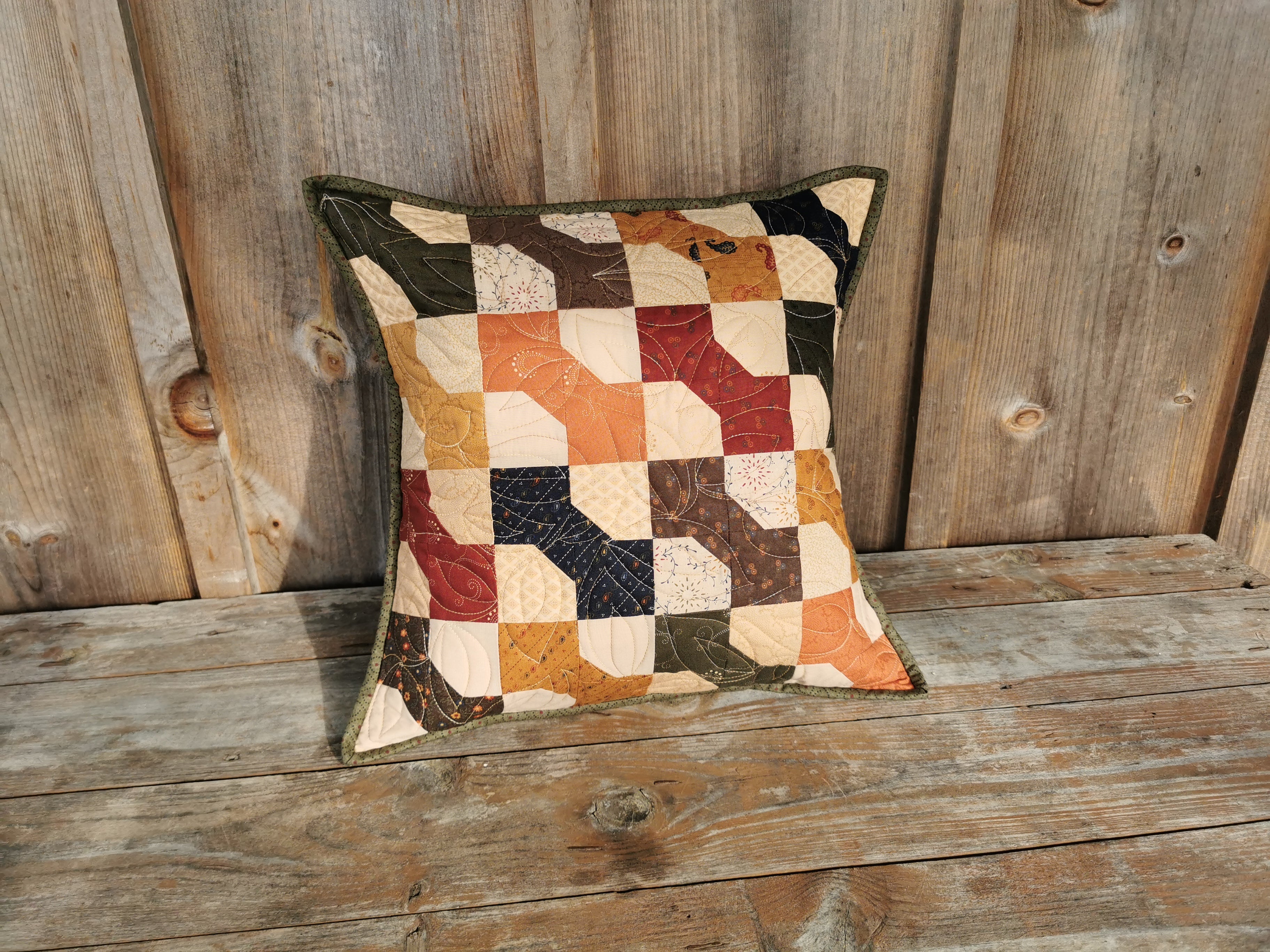 This quilted toss cushion has a country feel with the colorful bowtie patchwork. Bowties colors are: navy, brown, burnt orange, forest green, antique gold and country red. The beige background has a scrappy look using various coordinating fabrics. A lovely, rustic country look.