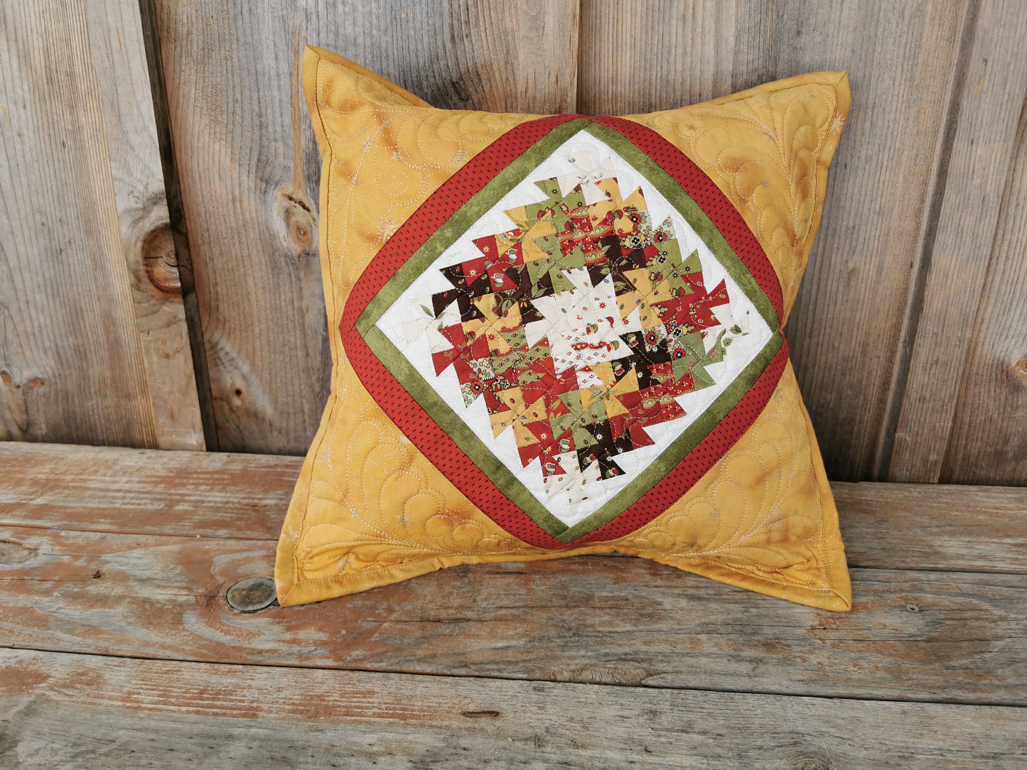 This patchwork pillow features intricate little twisters, in a wreath shape, in the center area. Framed by borders in green, red and gold that mirror the twisters makes for a eye catching, coordinating cushion. 