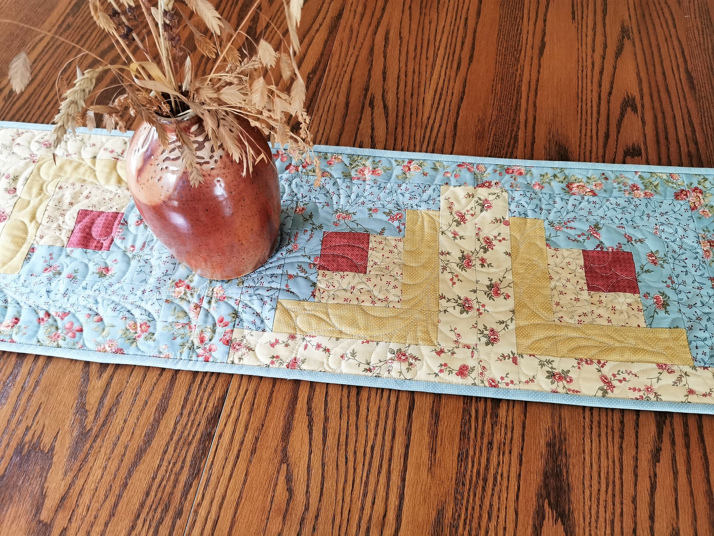 This pretty floral log cabin table runner is done in a soft teal blues and golden yellows with a touch of coral pink. Very pretty.