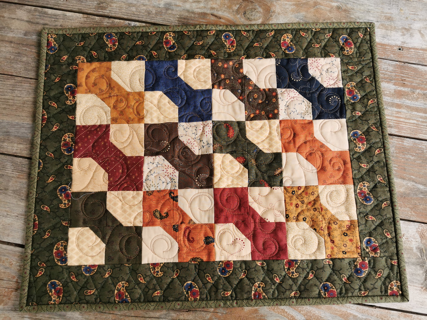 The quilted table runner with bowtie patchwork is shown from overhead.  Each bowtie is a different colour creating a lovely scrap quilt. The rich dark colors and country floral fabrics make this a  lovely, rustic decor piece for fall.