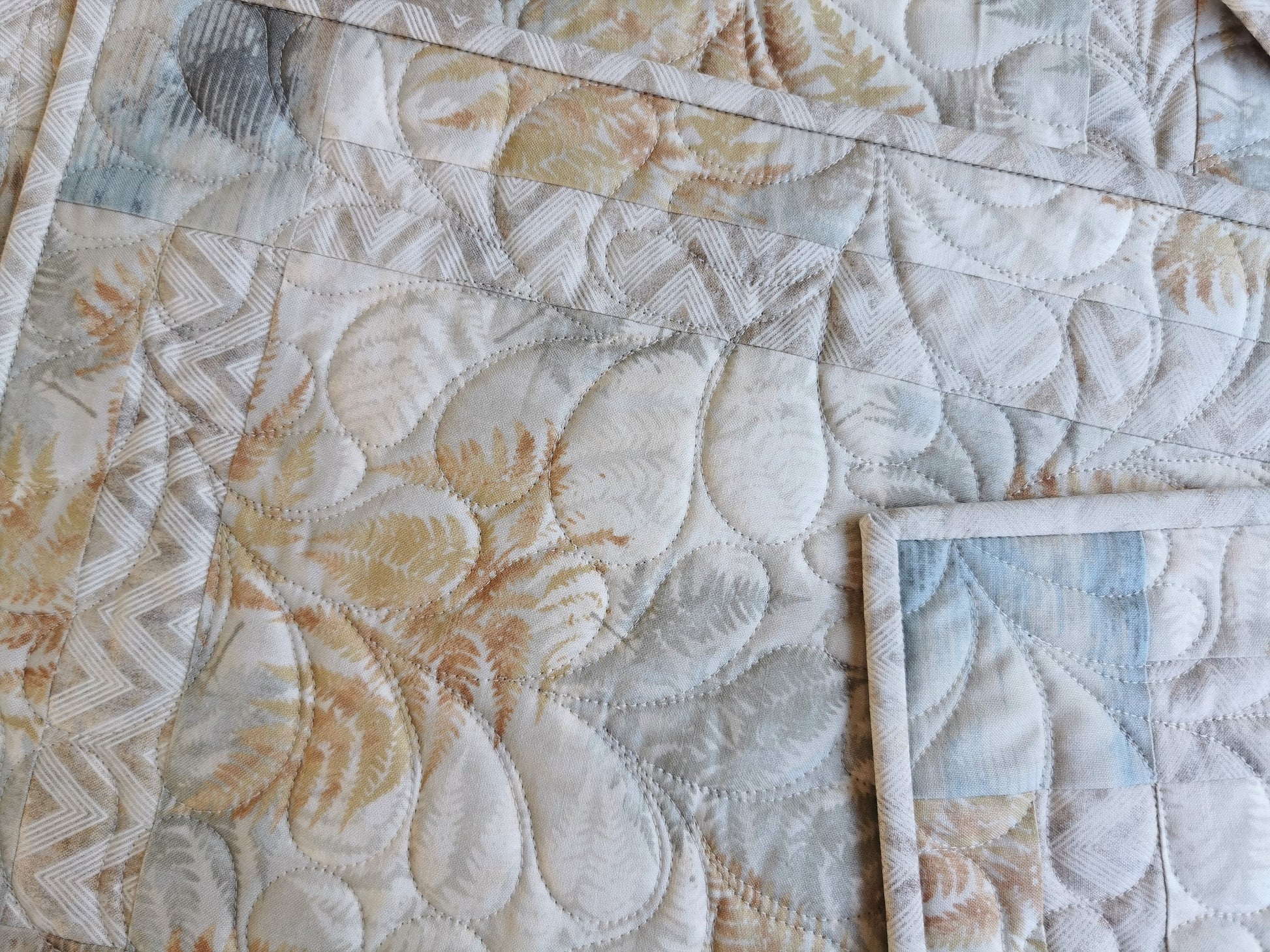 close up of the quilted placemats showing the abstract ferns in beige and slate blue.