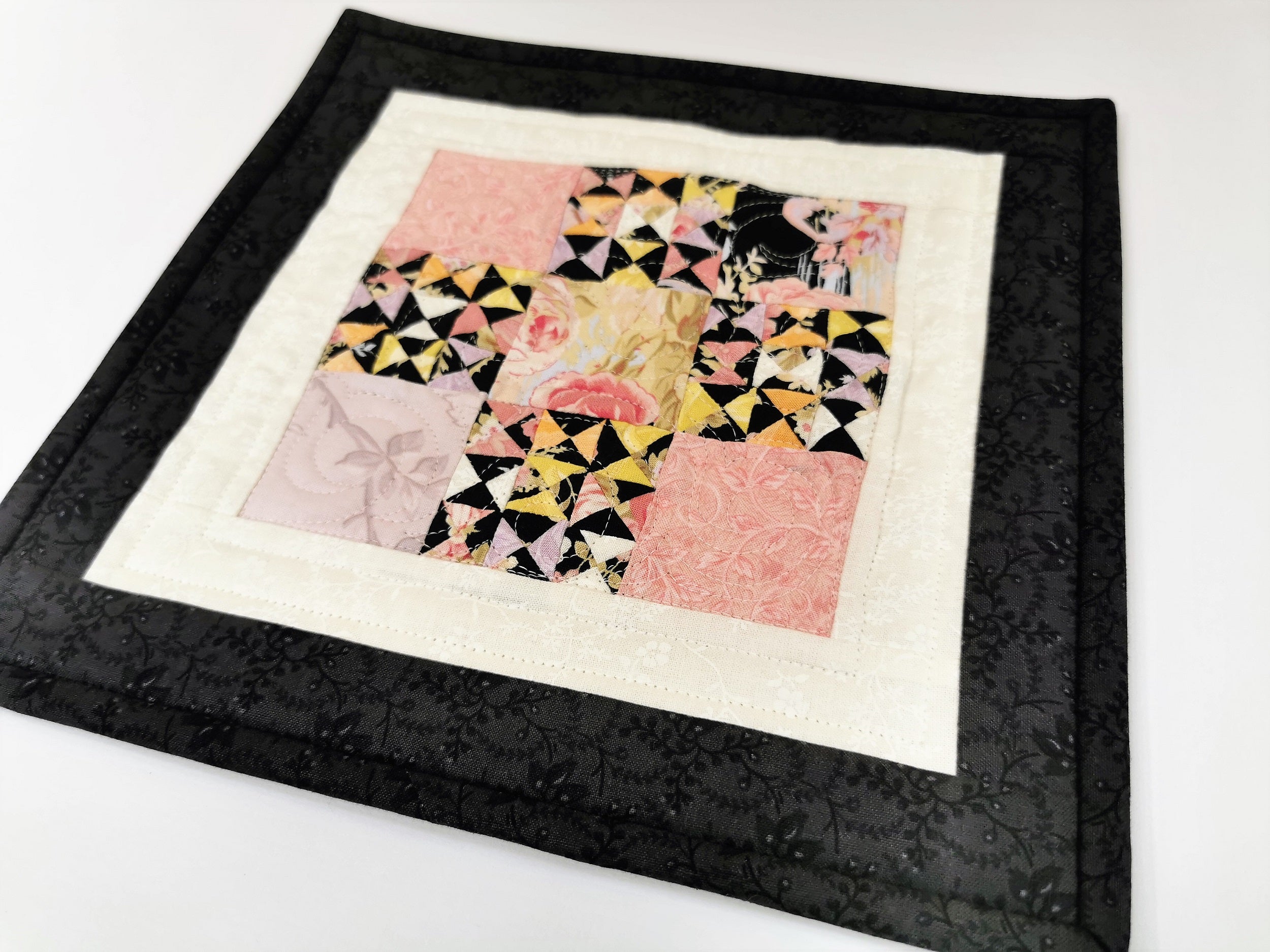 This improv mini scrap quilt features soft pastels paired with dramatic black and white borders. A great little mug rug or candle mat.