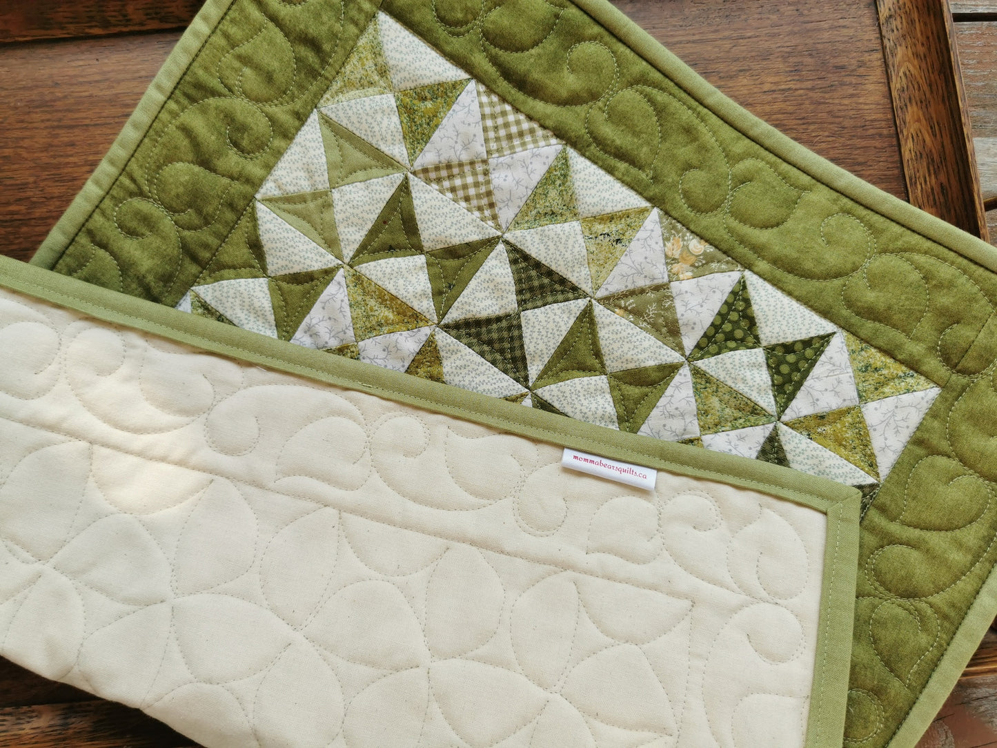 The green patchwork runner is shown on a wooden tray and folded to show the backing which is a plain, off white muslin.