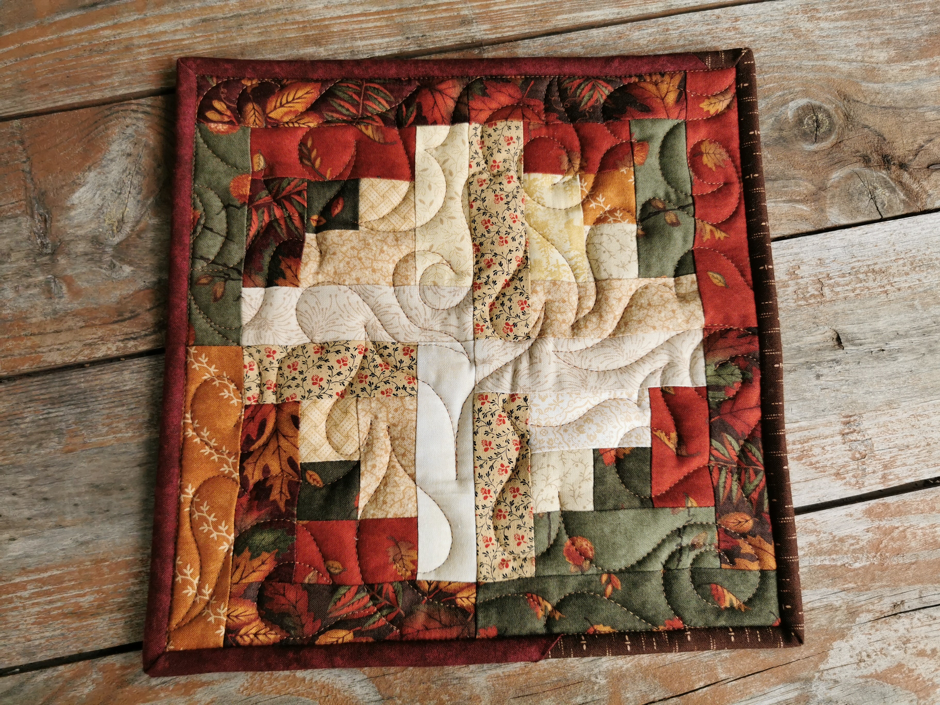 this rustic quilted potholder features log cabin patchwork in cotton prints of fall leaves. Colors include brown, tan, gold, green, rust, red, light beige & cream.  A large size kitchen hot mat.