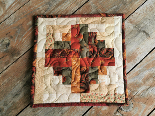 this large patchwork potholder is done in a log cabin quilt style. Cotton fabrics are a fall leaf theme with colors including brown, rust, green, gold, red & beige