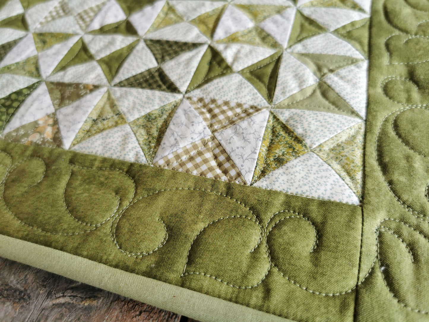 A close up shot of the quilted table runner showing stitching detail and leafy vine border stitching. 