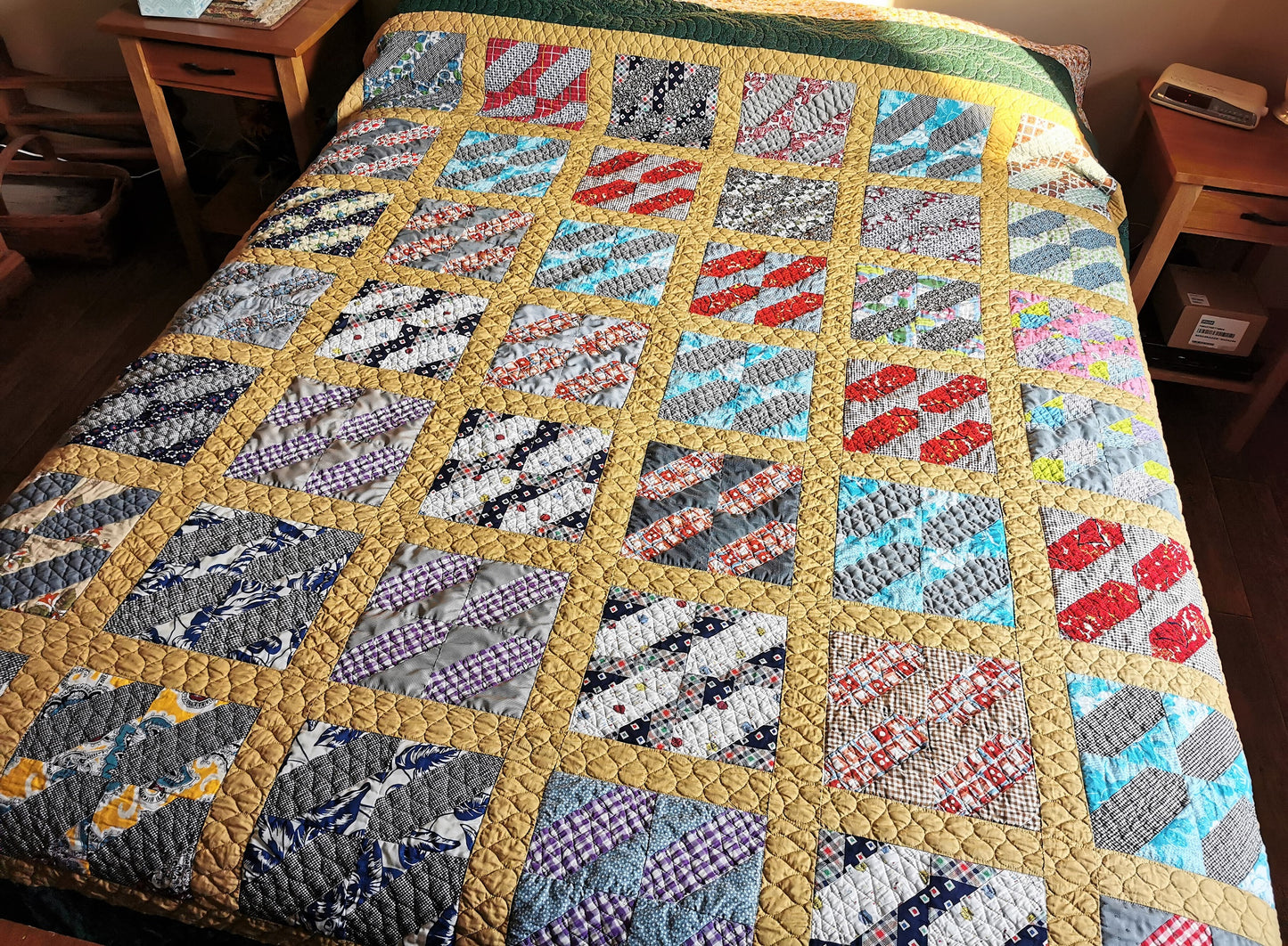 the vintage patchwork blocks in the mustard yellow grid is shown here. Each block within the grid has vintage fabrics and is made of basically two colors with the piecing done in such a way as to create the effect of four backslashes in each block. Colors include various shades of gray, red, lighter blue, navy, a touch of yellow & purple.  