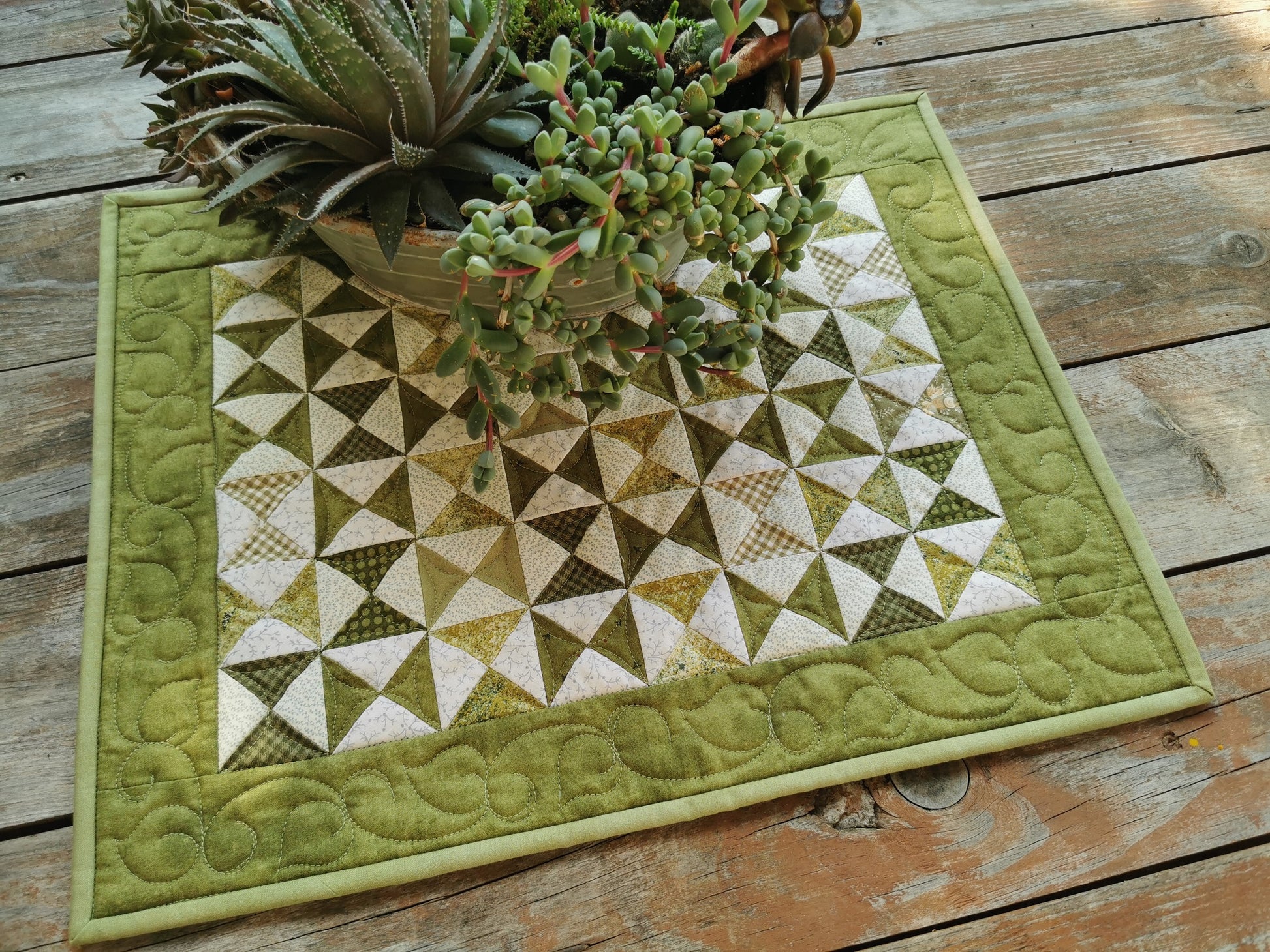 the quilted table runner is shown in a lifestyle shot , in natural outdoor lighting with a planter of succulents sitting on it. 