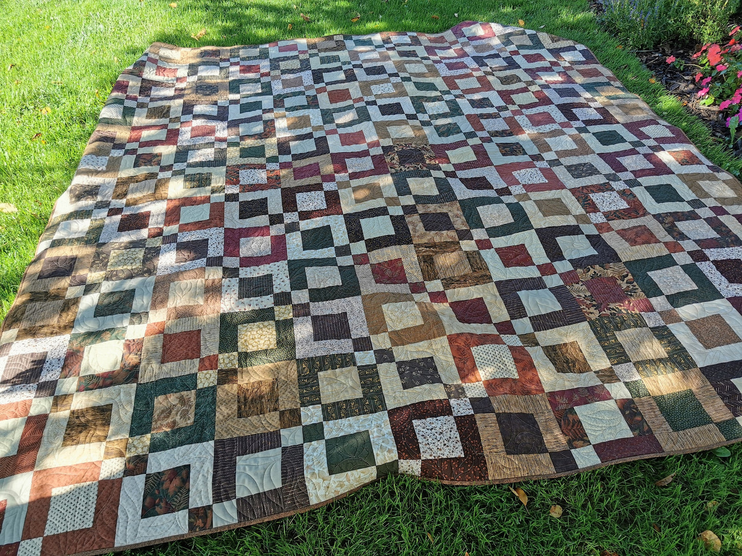 quilt shown outdoors on the grass in dappled shade.