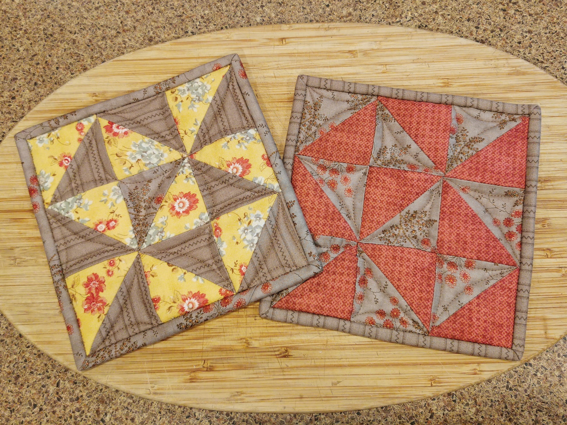 the quilted patchwork potholders are shown in indoor light which minimizes the quilting texture and allows the patchwork to become predominant, showing the pinwheel piecing and the tan, coral and floral fabrics 