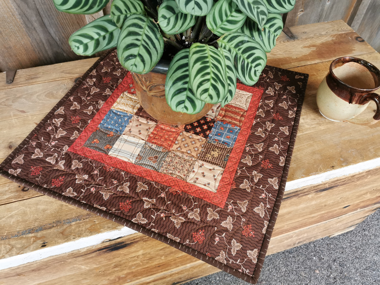 lifestyle shot of the quilted table topper on a wooden chest with a plant and coffee mug