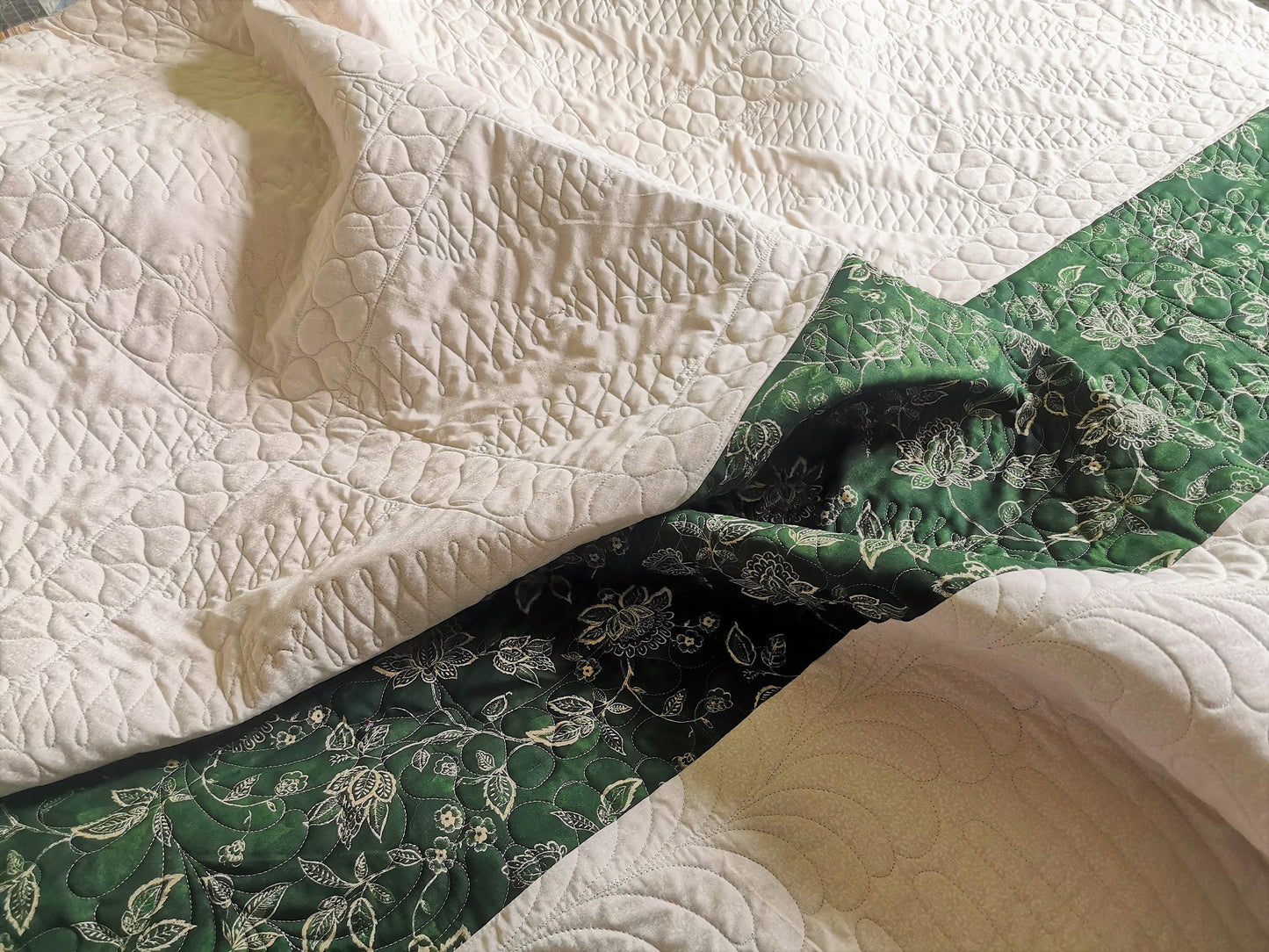 This shows the back of the vintage bed quilt. the backing is a tone on tone ecru print with a dark green stripe pieced across the one end. Stitching detail is easily seen on the back. 