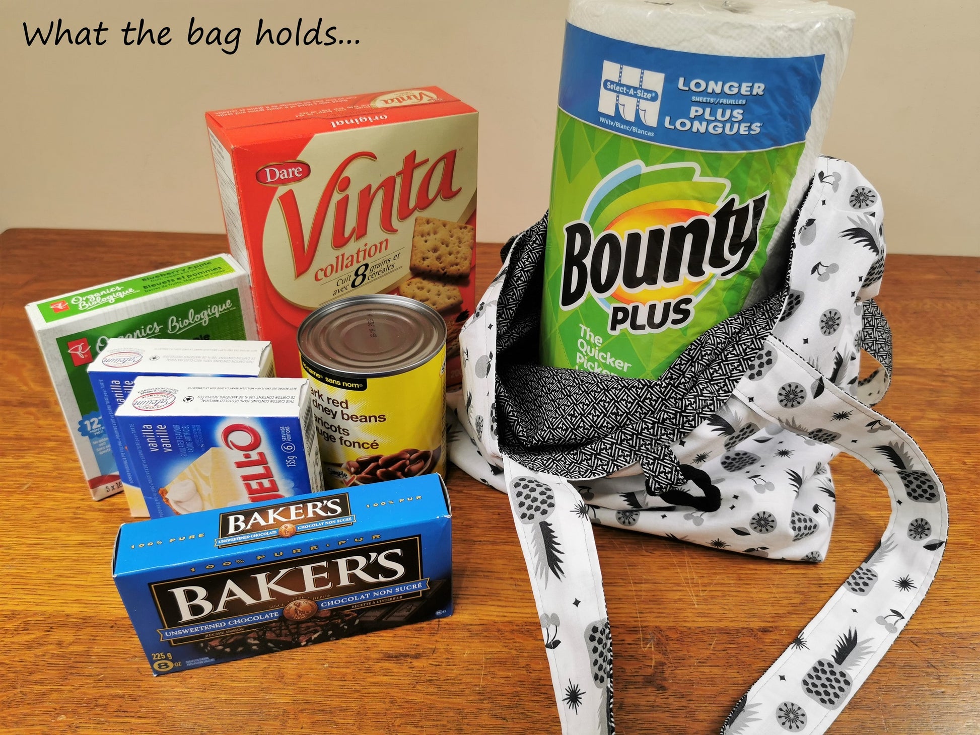 Image shows that the bag holds the following grocery items: Large roll Bounty paper towels, box Vinta crackers, can of kidney beans, two boxes of Jello pudding mix, small box fruit snack bars, box of Bakers unsweetened chocolate squares.