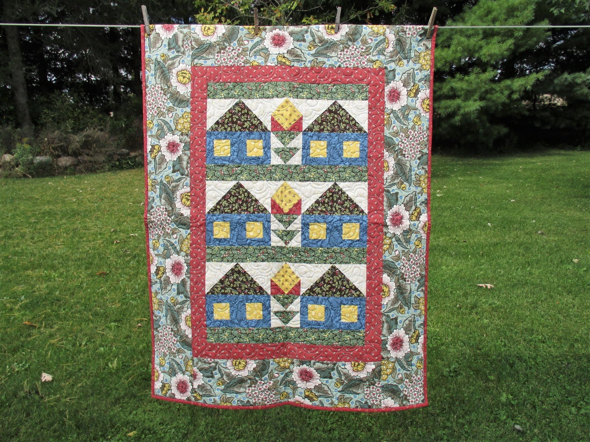 this large wall quilt has six patchwork houses set with a flower in between in three rows of two. 