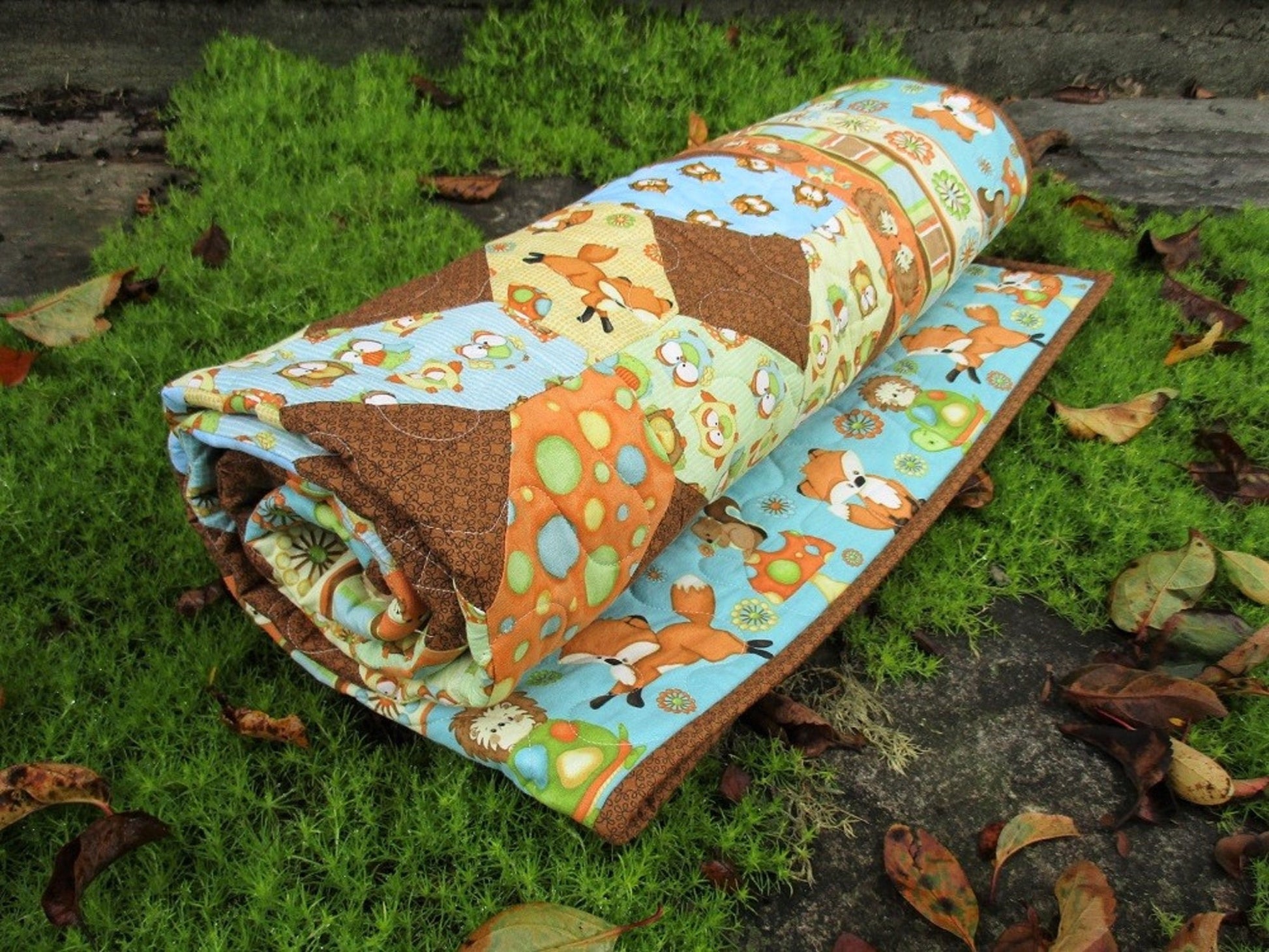 rolled baby quilt outdoors on moss with fall leaves around