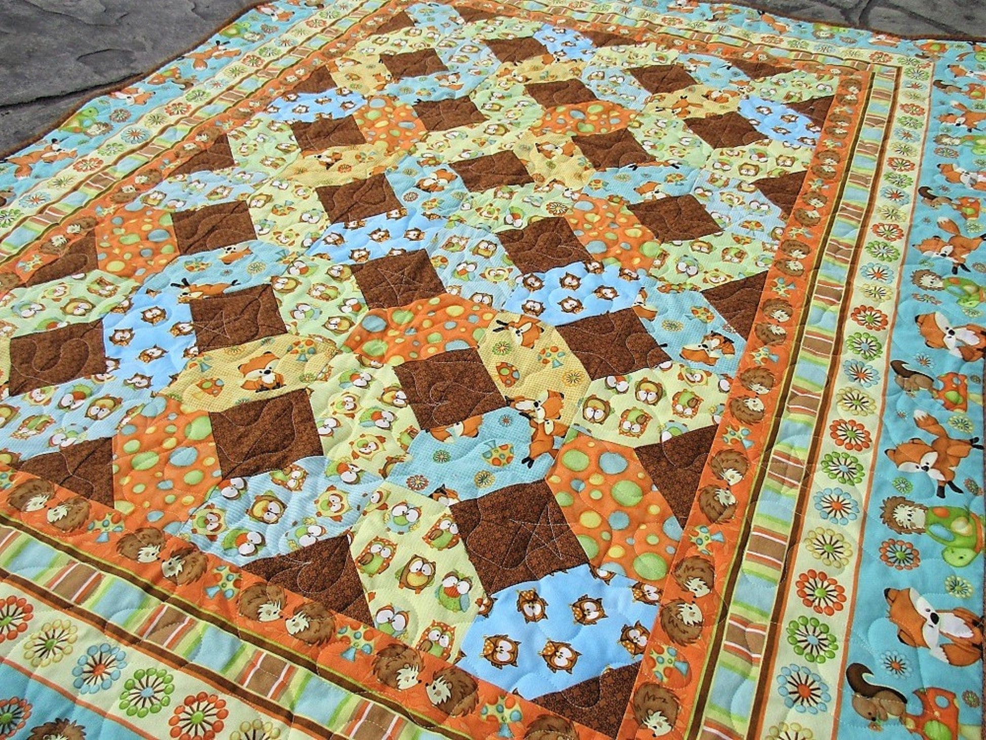 angle view of the baby quilt showing the lattice pattern in the middle and coordinating fabrics. See baby owls, hedgehogs, foxes, colorful polka dots, stripes and more.