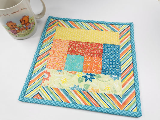 quilted mug rug in summery cheerful prints in shades of  blue, yellow, orange and teal. 