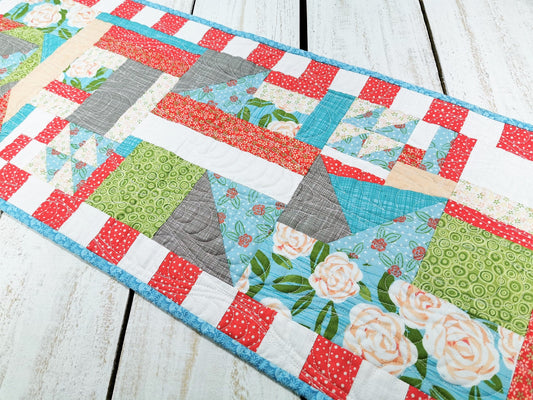 This summer table runner is made in a crazy quilt style. Colors are watermelon red, teal, clean white, spring green, peachy pink, and gray.  Many of the fabrics are floral, both large and small scale prints.
