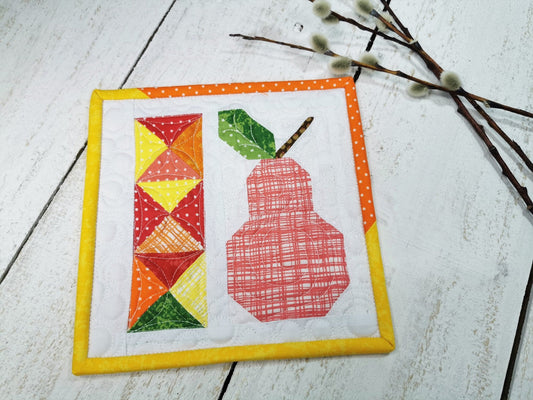 This scrappy patchwork pear quilt has primary colors on a white background. The pink pear with a stem and green leaf has very small pieces. Other patchwork colors are yellow, red, orange.
