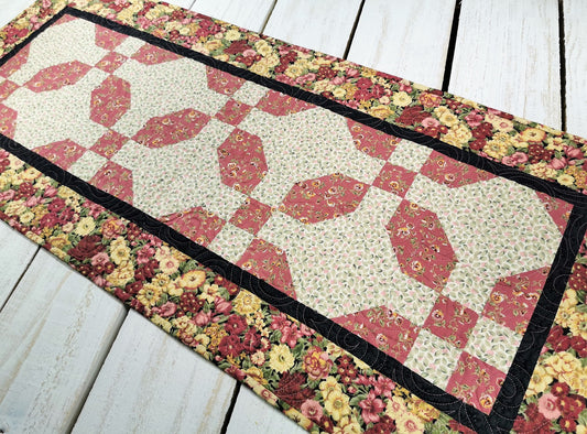 Lovely florals star in this table runner. Colors include deep rose pink, tan, cream, green and black. Even the patchwork piecing is done in a floral pattern. the outer border is a gorgeous larger scale floral print that incorporates all the colors. Predominant color of the runner is the deep rose pink.
