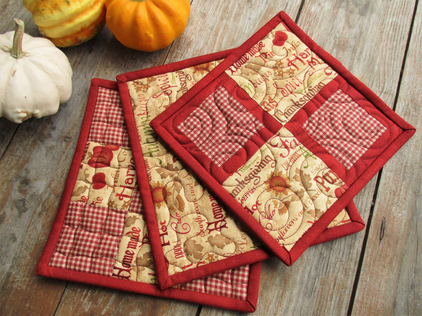 Three red gingham pot holders are functional and pretty. Thanksgiving and fall theme fabric is the focal point. 