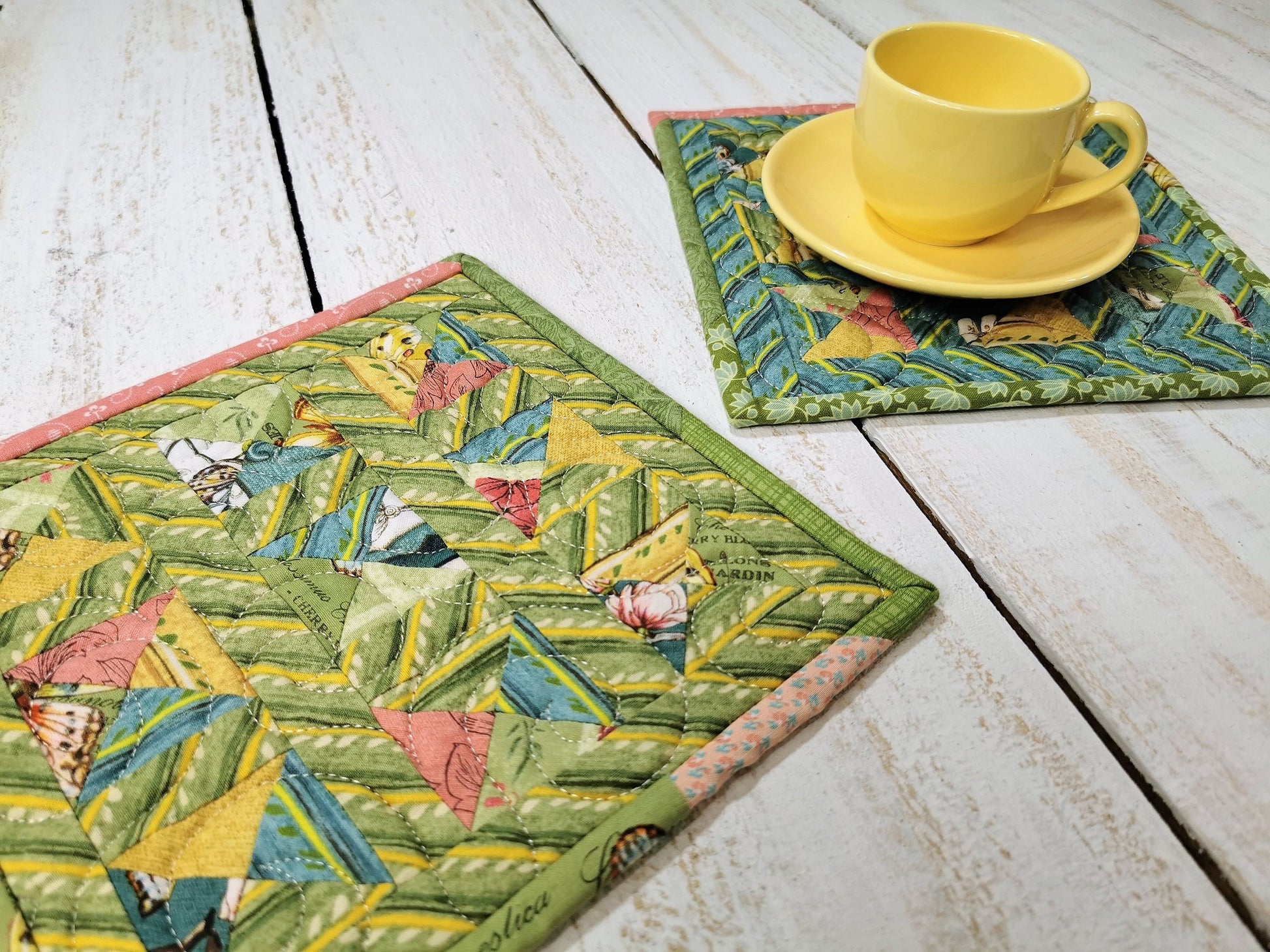 two potholders on white wooden table with small yellow mug and saucer in background