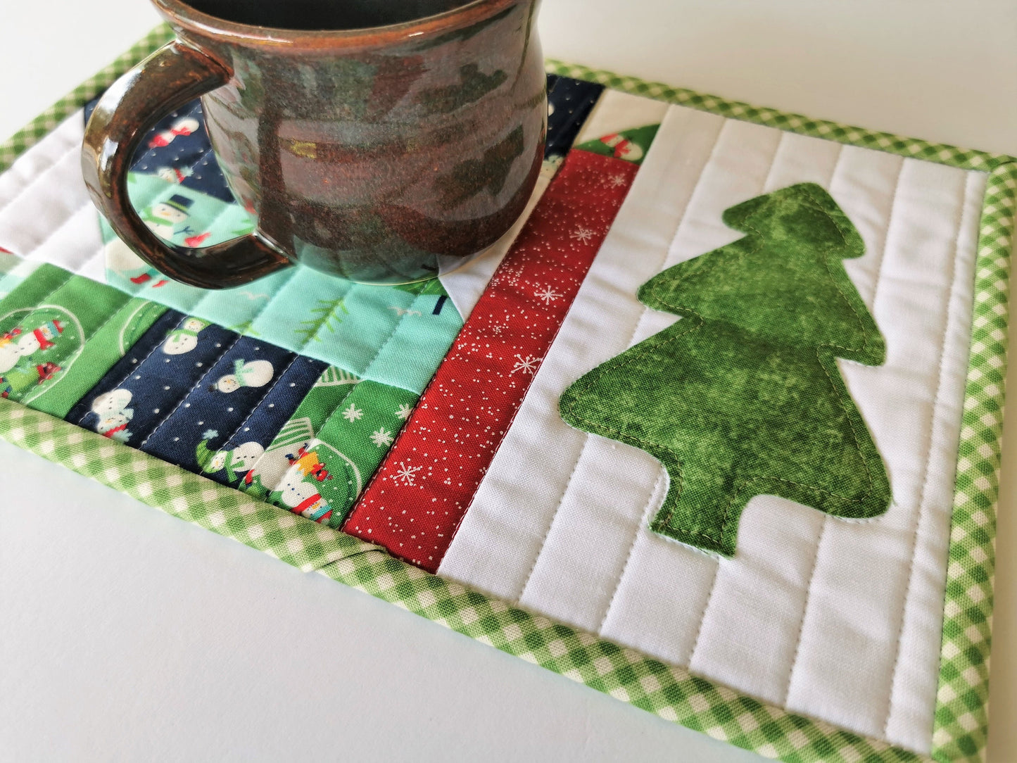 Winter theme fabrics in scrap quilt patchwork are a sweet compliment to the green christmas tree on this holiday snack mat, mug rug.